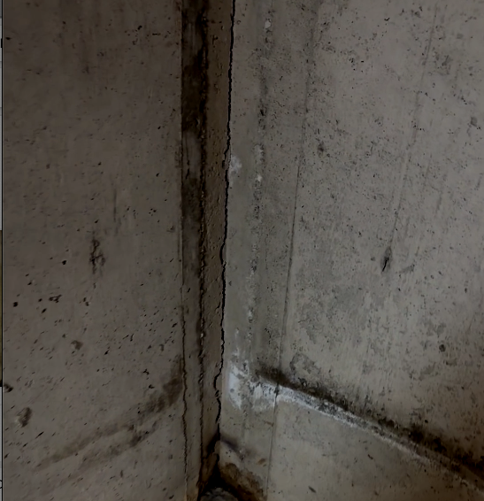 Coin de mur en béton avec une fissure et des taches d'humidité.