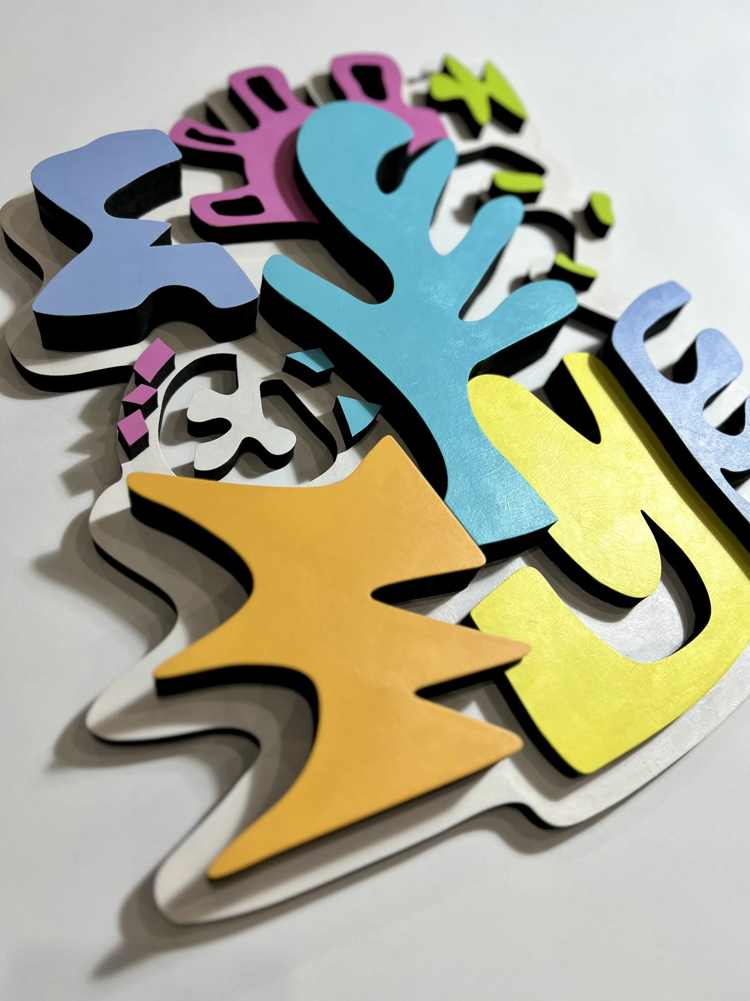 Colorful 3D wooden cutouts of letters and shapes layered on a white surface.