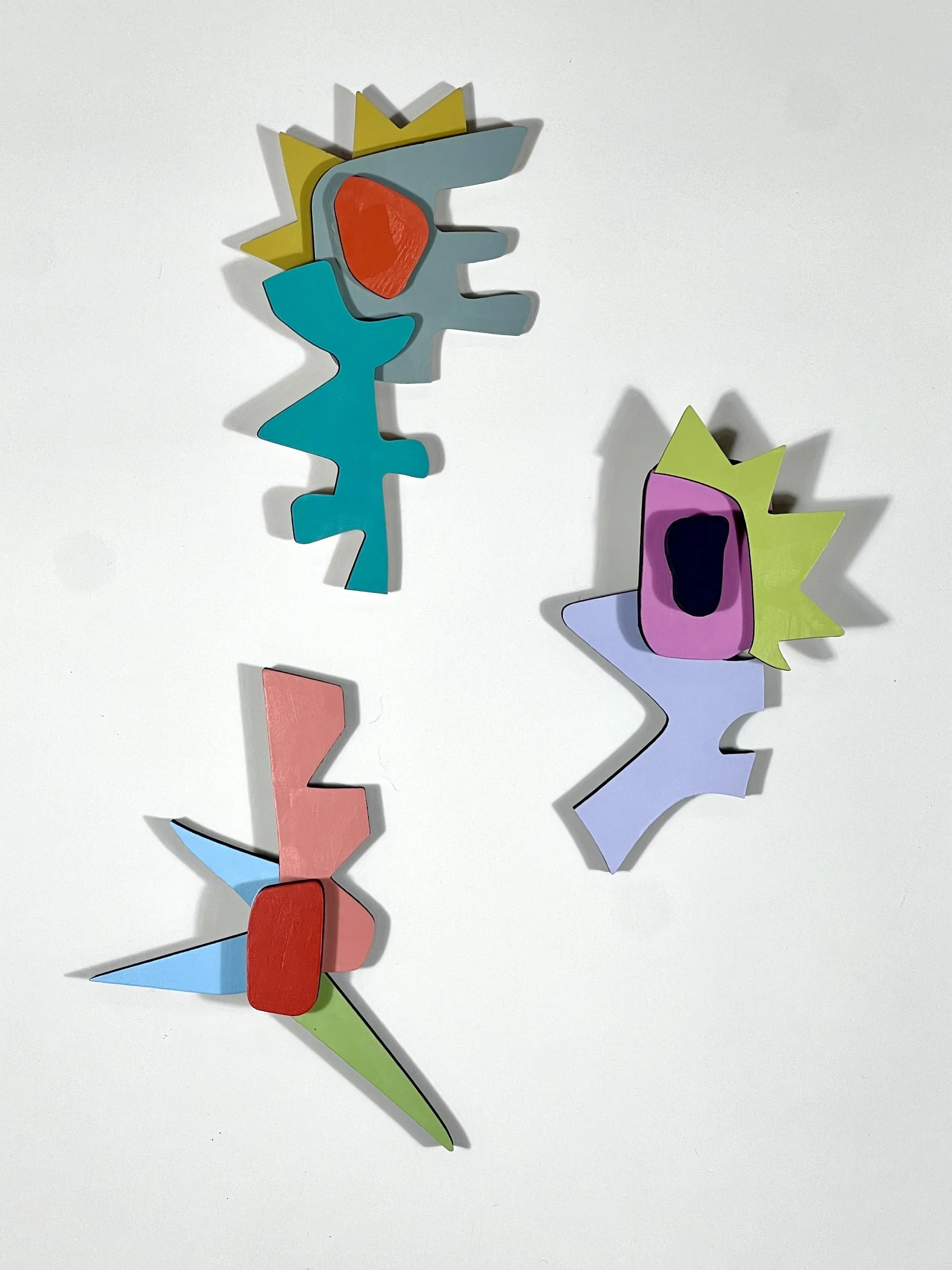 Three abstract, colorful, geometric wooden wall art pieces with jagged edges and bold colors, arranged on a white background.