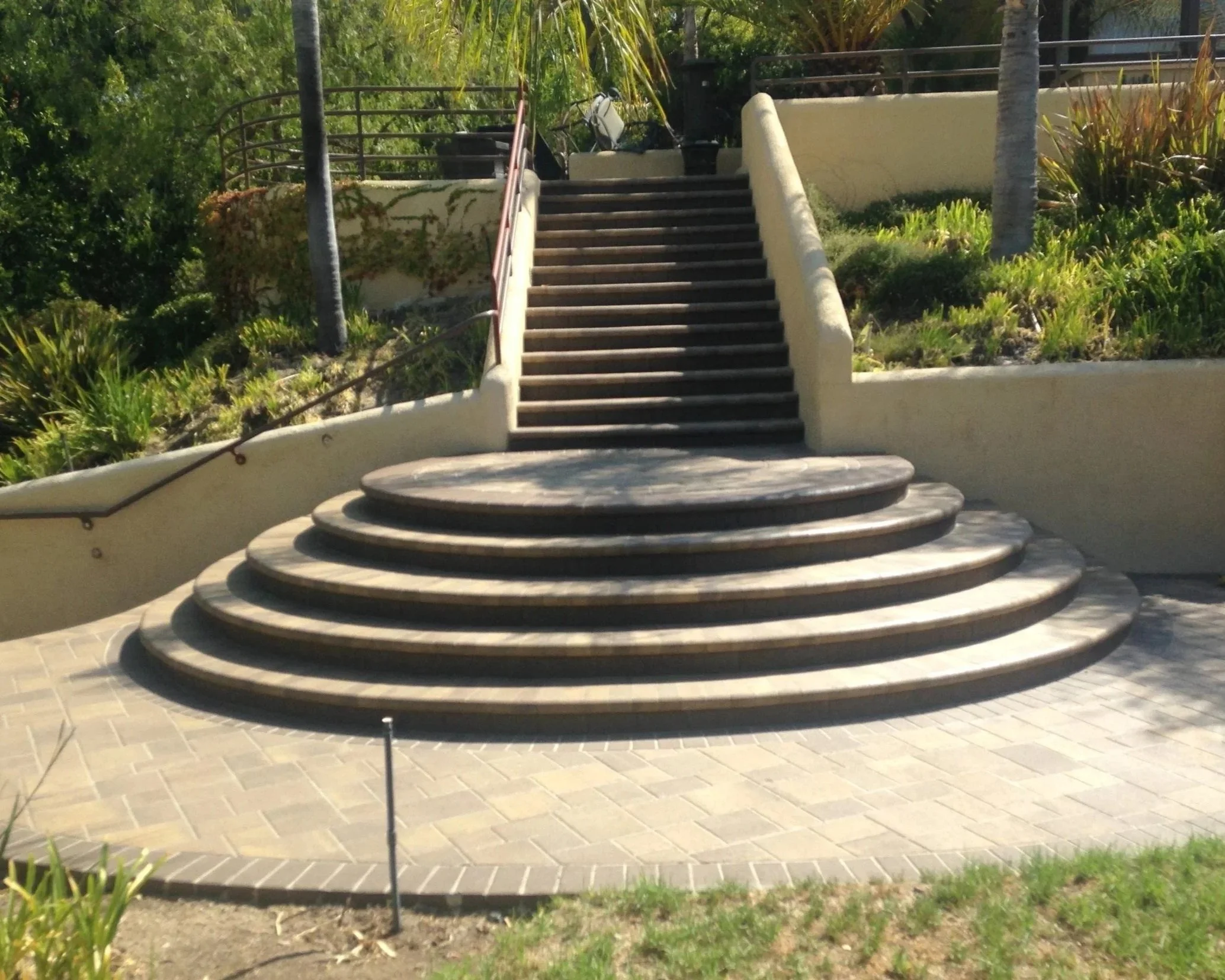 Outdoor staircase with multiple steps leading up to an elevated area, surrounded by plants and trees.
