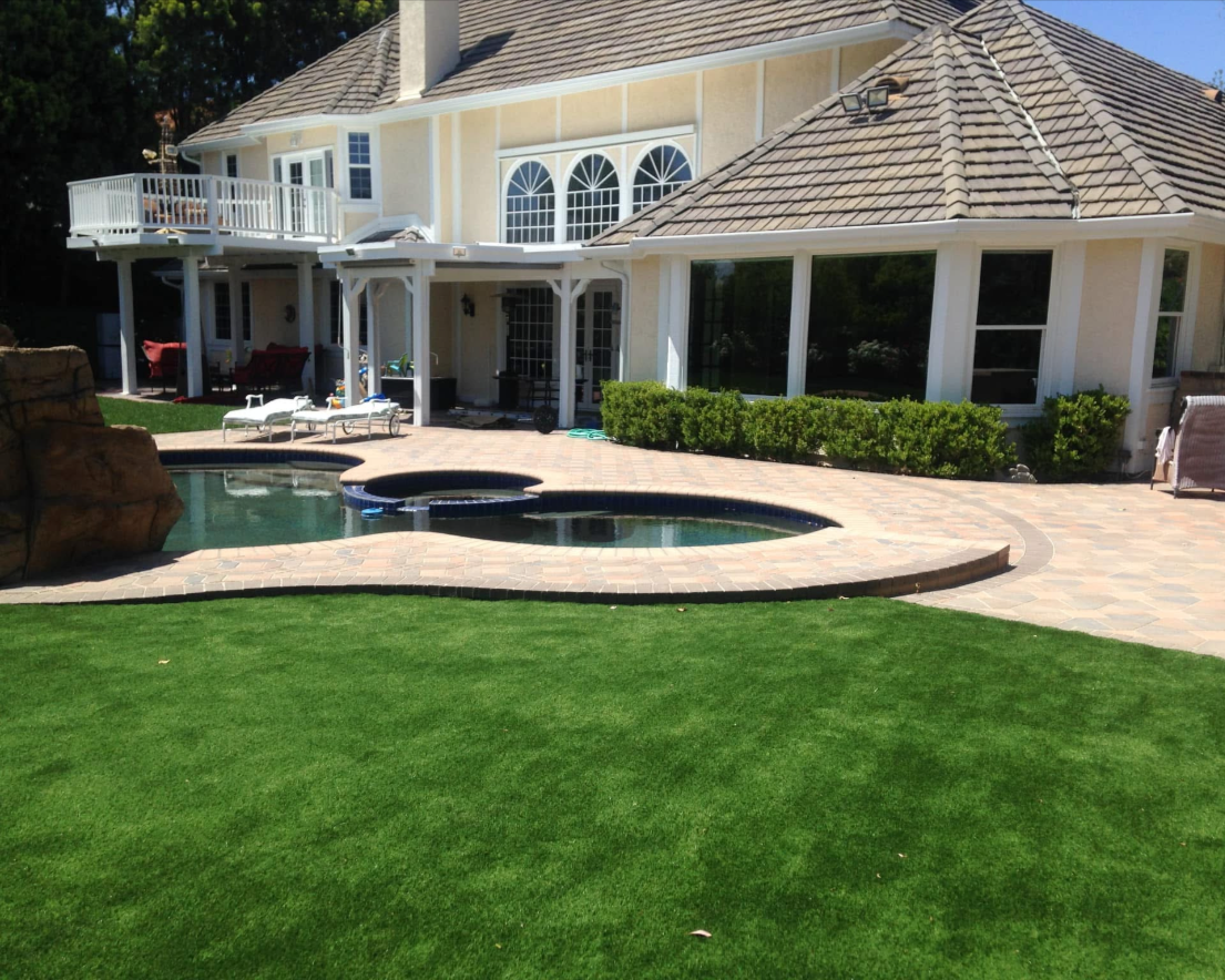 Backyard with swimming pool, hot tub, paved patio, green lawn, house with large windows and balcony.
