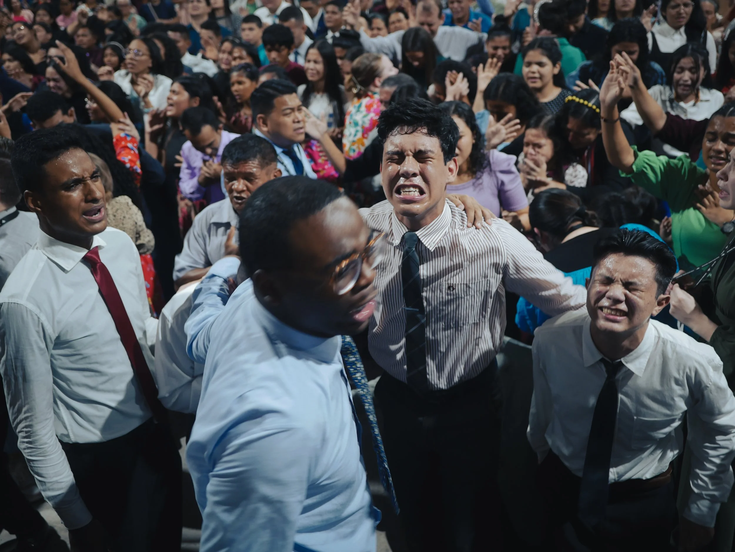A large crowd of people, mostly young, appears to be in a moment of distress or emotional intensity, with many looking upset or crying and some clutching each other.