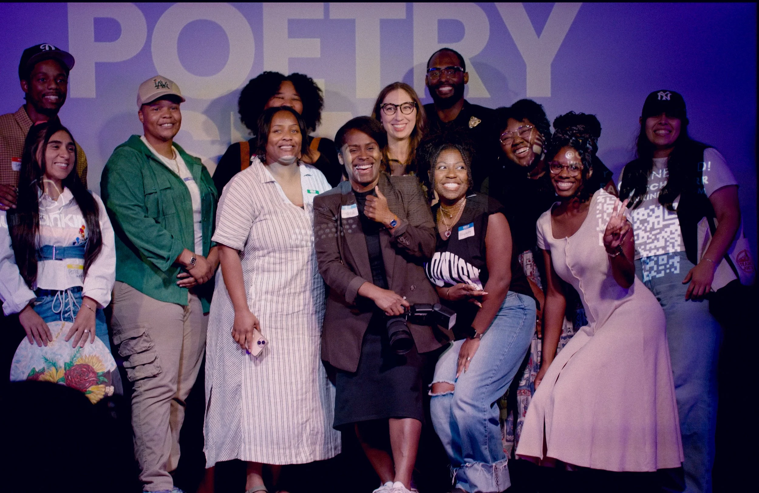 A diverse group of christian craetives in austin texas smiling and posing together at an event with a large sign that says 'christian arts POETRY slam' in the background.