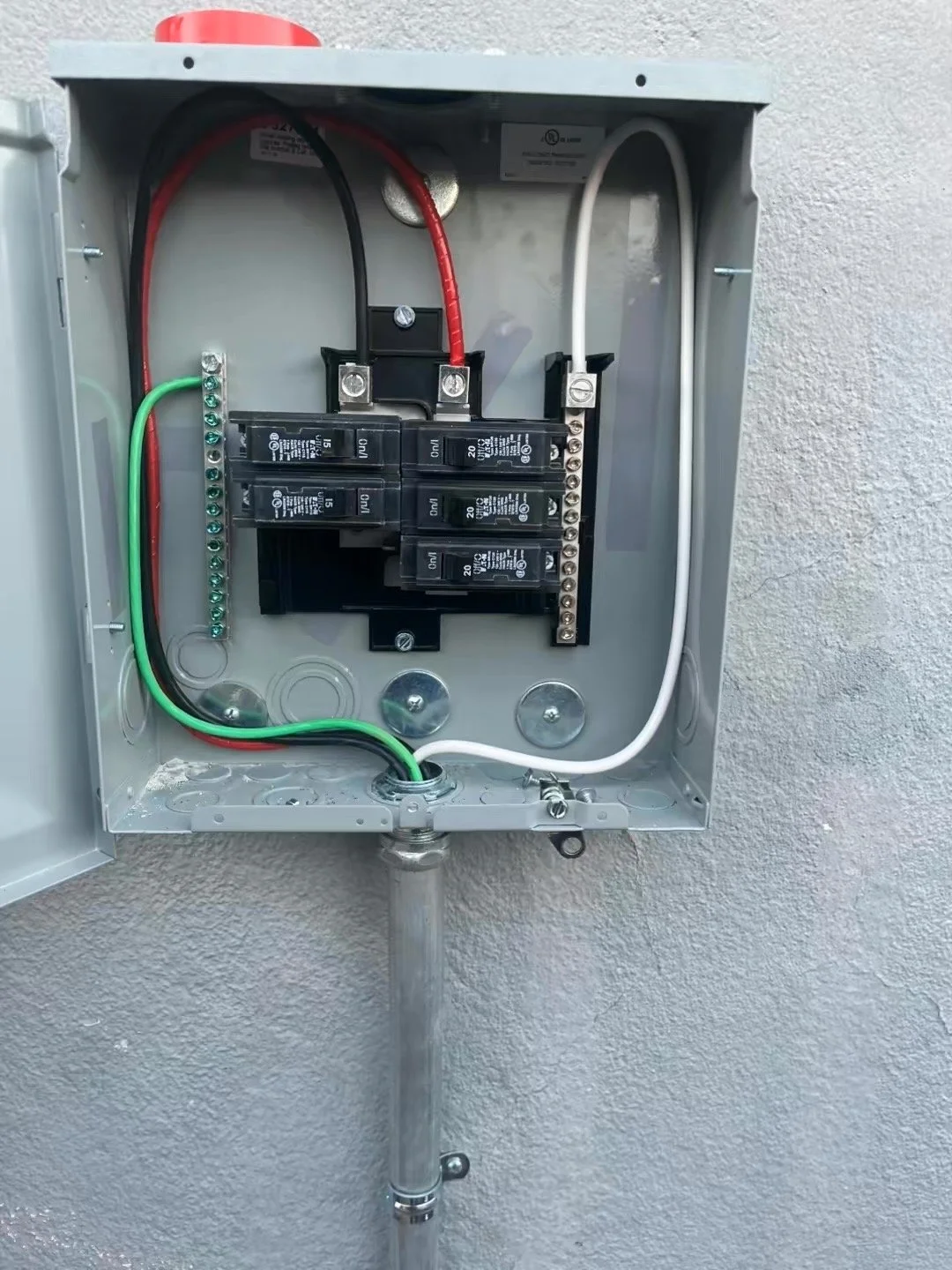 An open electrical panel box with circuit breakers and wiring on a gray wall.