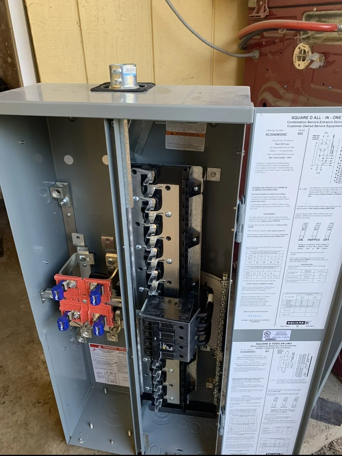 Open electrical panel with circuit breakers, red and blue wire connectors, and wiring visible inside the metal box.
