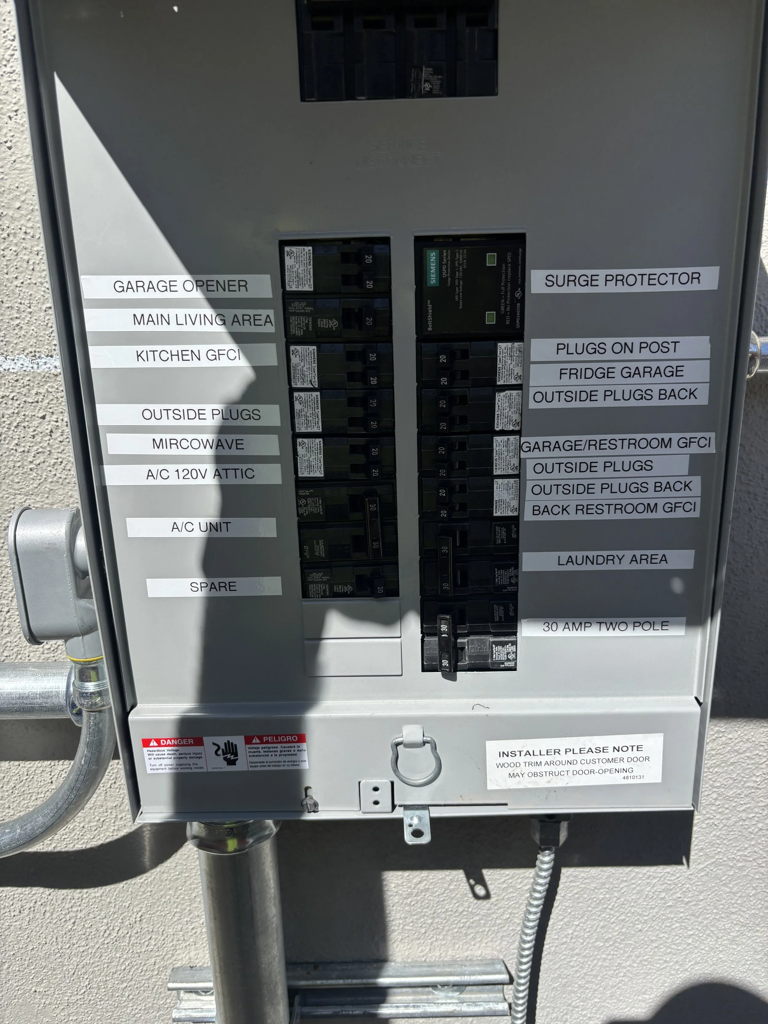 An electrical circuit breaker panel with labels indicating different circuits such as garage opener, main living area, kitchen GFCI, outside plugs, microwave, attic air conditioning, and additional circuits for appliances, outdoor outlets, bathrooms,