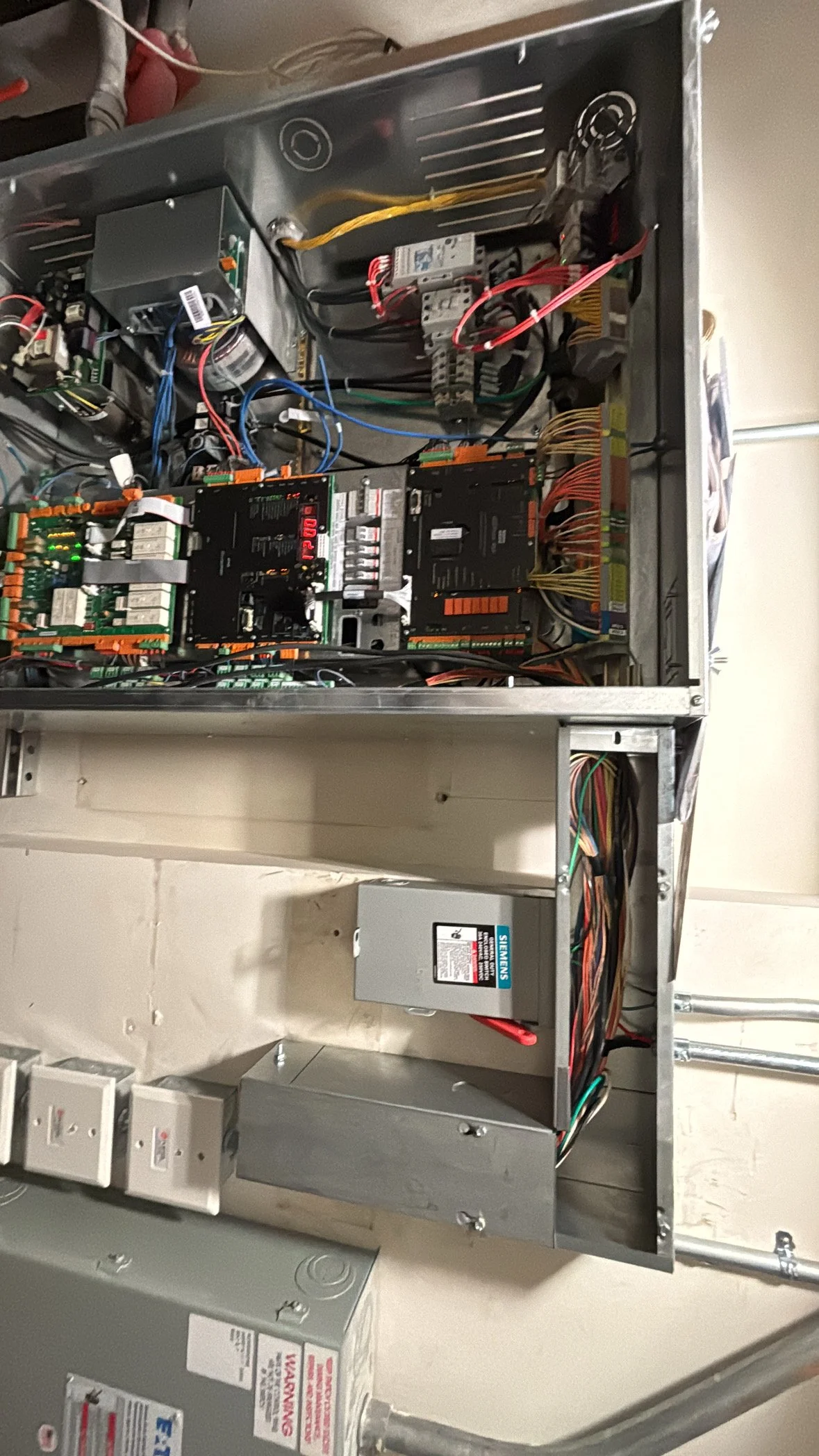 Open electrical control panel with various components, wiring, circuit boards, relays, and a Siemens power supply unit inside a metal enclosure.
