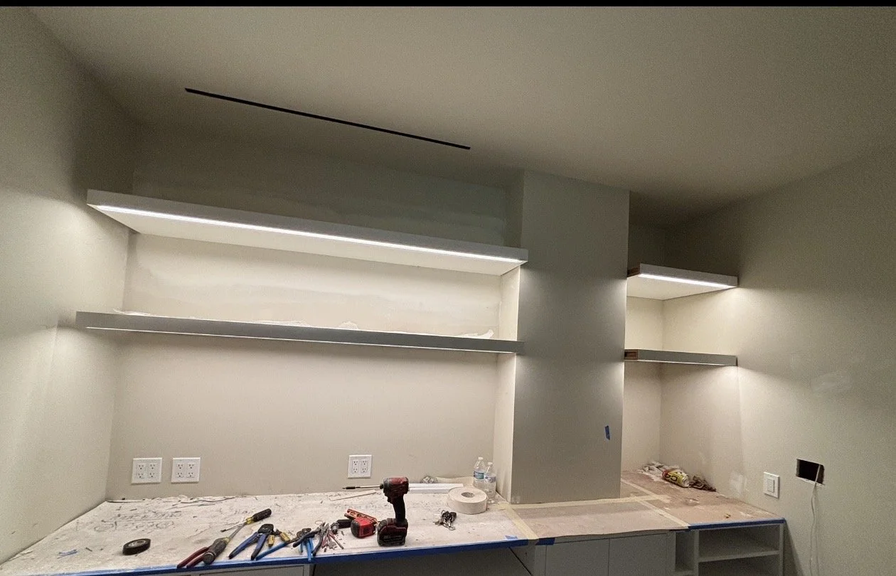 A kitchen or workspace under renovation with open shelves on the wall, some tools and supplies on the counter, and electrical outlets installed.