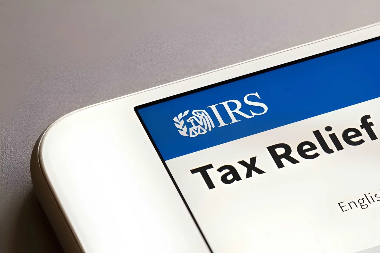 Close-up of a smartphone screen displaying the IRS Tax Relief logo with the text "Tax Relief" in bold, black letters. The background is a plain, neutral color.