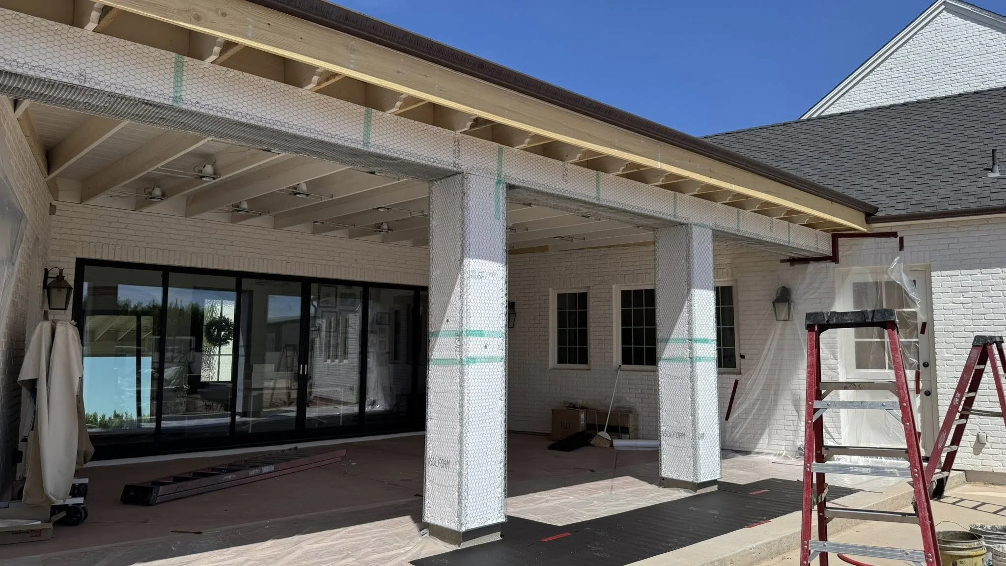 Construction of a covered patio extension with support columns, ladders, and building materials visible.