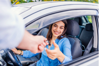 A woman in a blue shirt smiling and shaking hands with a person outside a vehicle.
