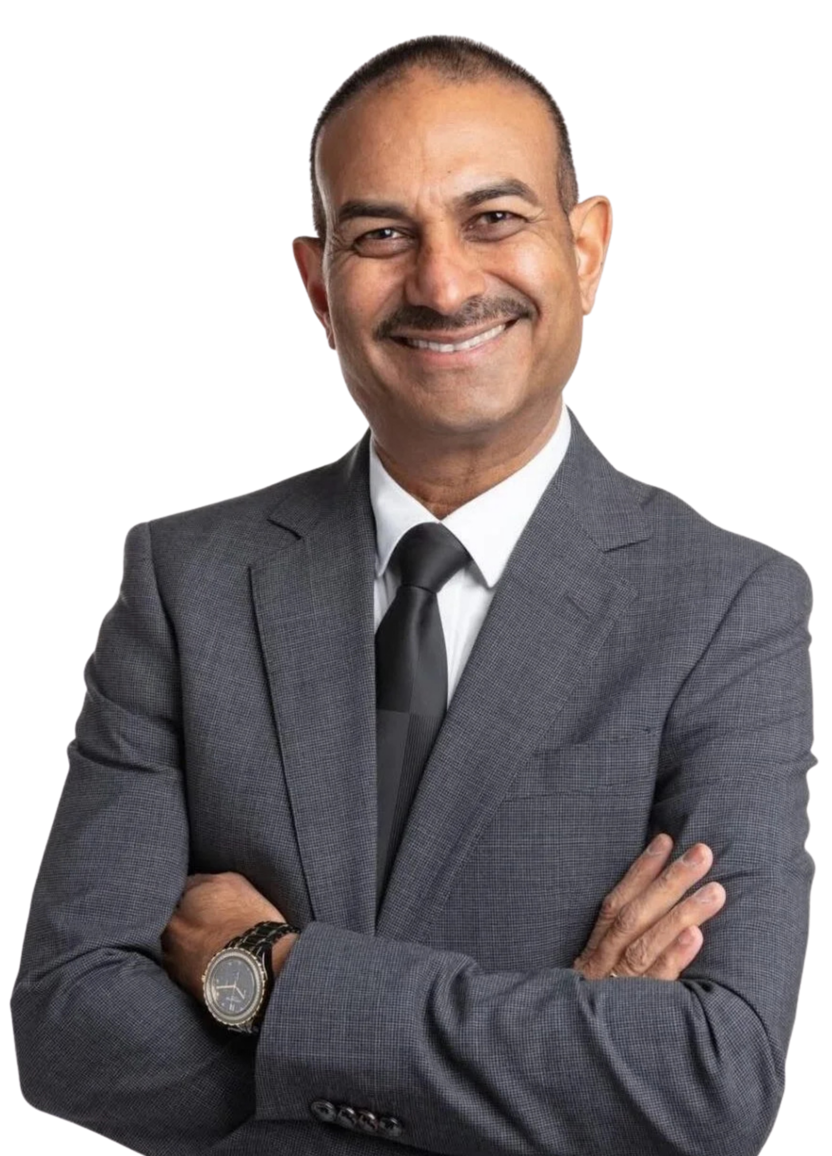 A smiling man in a dark grey checkered suit, white shirt, and black tie, with short hair, mustache, and a wristwatch, standing with arms crossed.