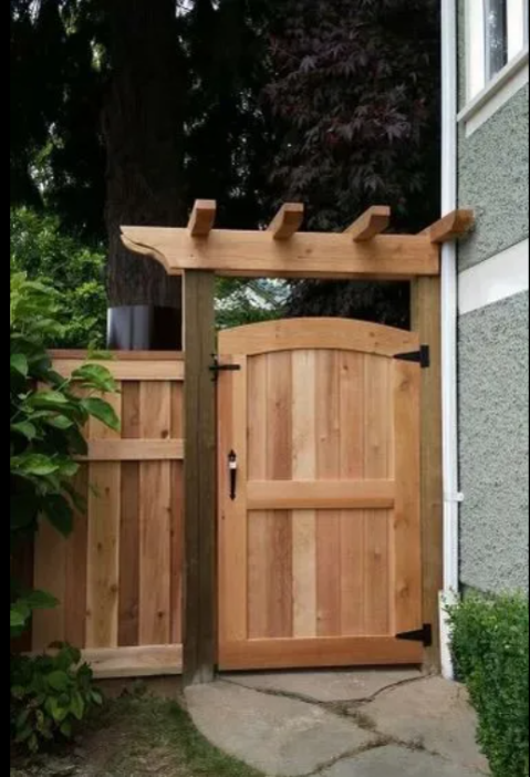 Wooden garden gate with trellis, attached to a fence, next to a house wall, in a backyard with greenery.