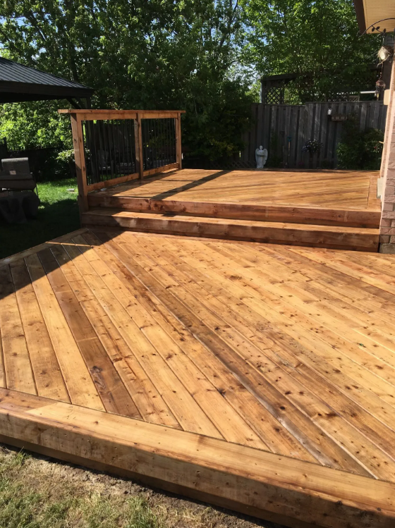 Newly built wooden deck with two levels, stairs, and railings in a backyard with trees.