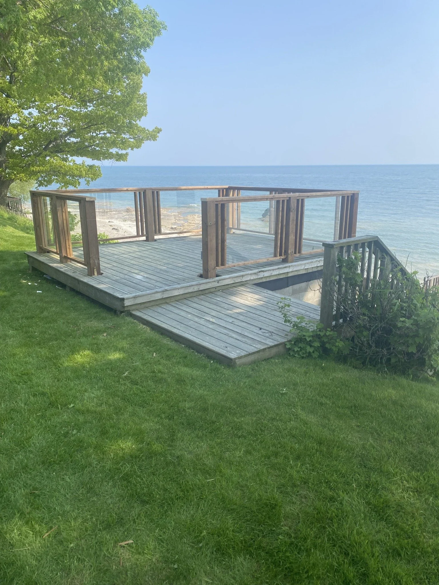 Wooden deck overlooking the ocean with a railing and a large green tree on the left side.