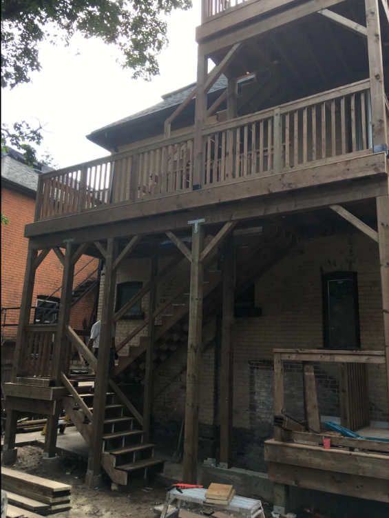Wooden deck or balcony construction on an outdoor building, with stairs leading up to it and construction materials nearby.