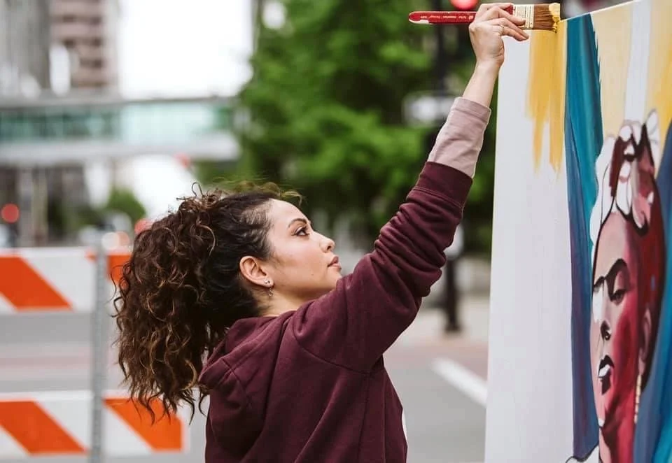 Woman painting a colorful mural on a large outdoor wall.