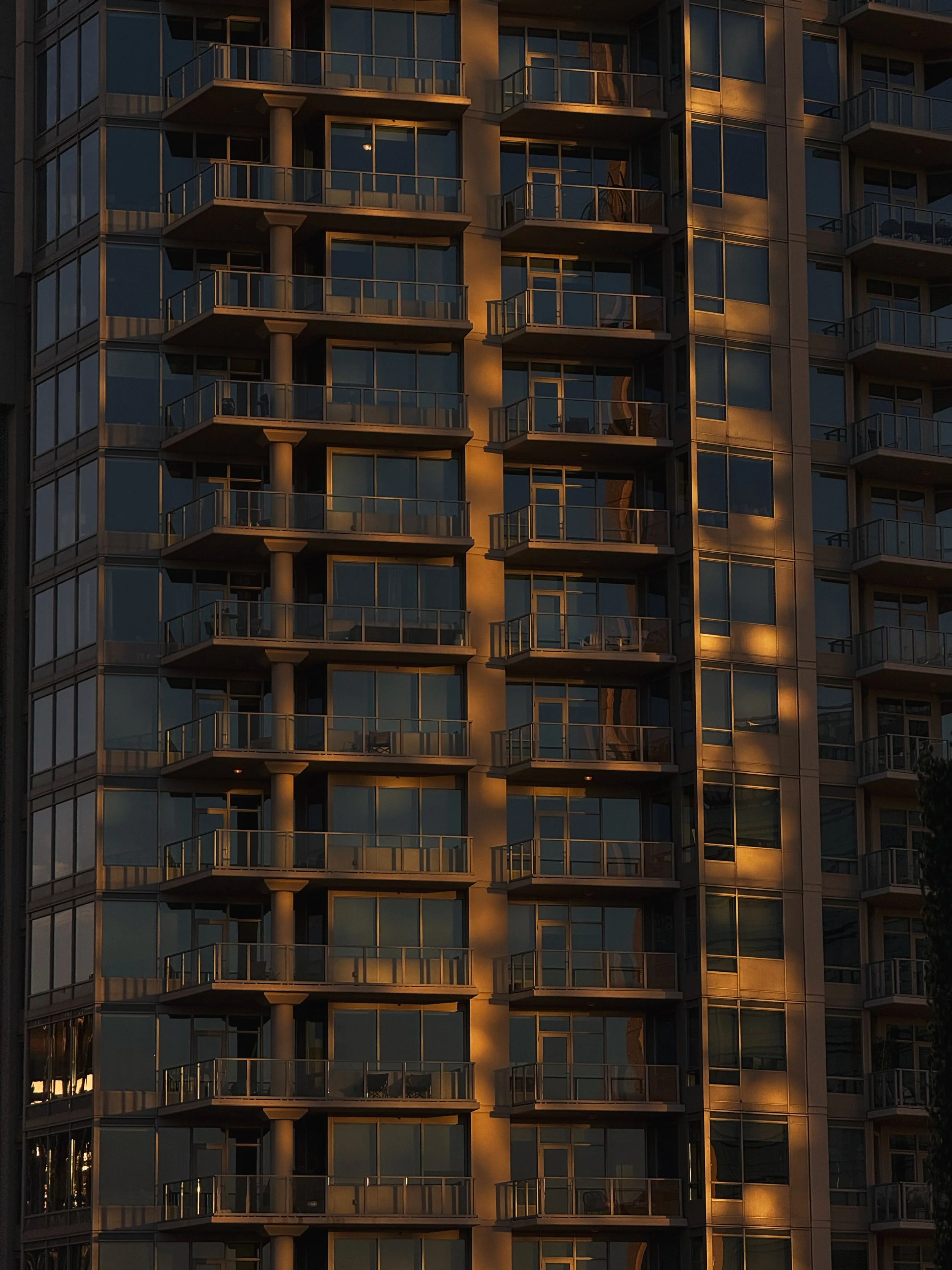 Close-up of a modern high-rise apartment building with glass balconies reflecting warm sunset light.