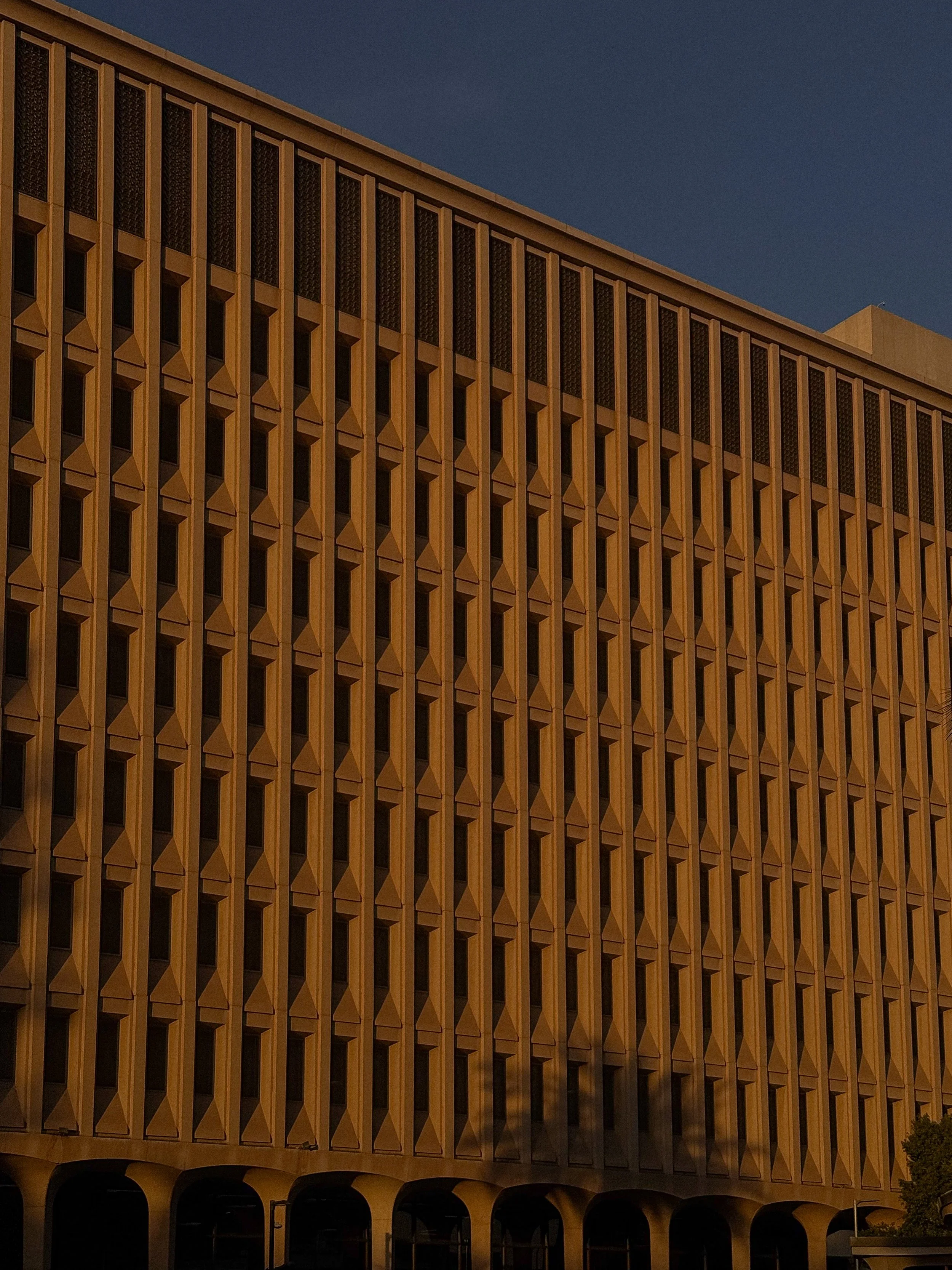 A large building with a geometric facade and multiple vertical rectangular windows, seen against a dark sky.