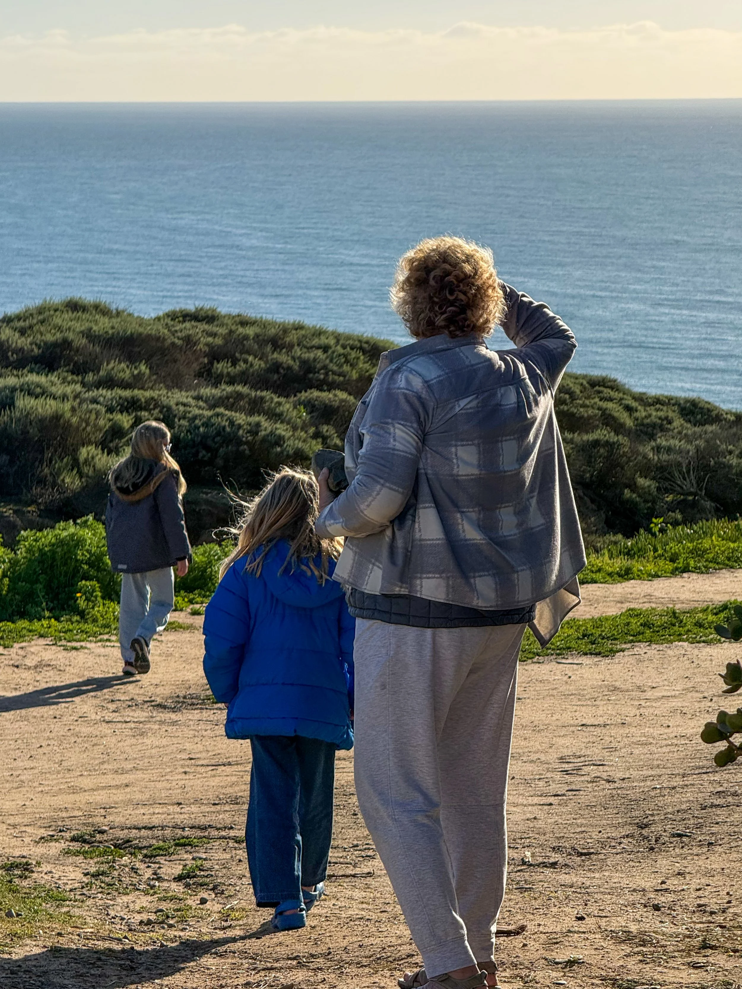 Woman and two children walking along a coastal trail, with one child and the woman looking out towards the ocean.