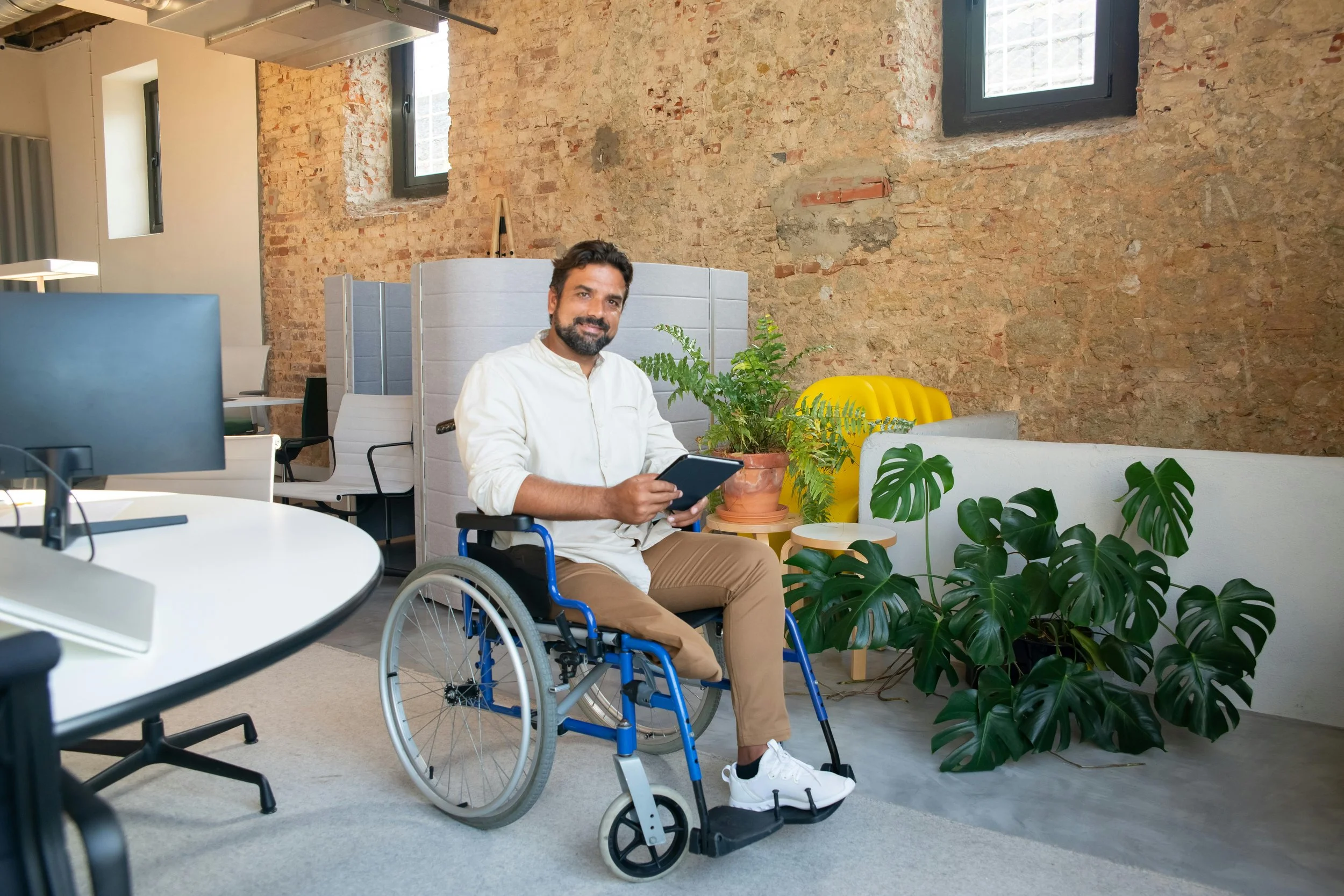 Man using wheelchair in office, smiling at camera.