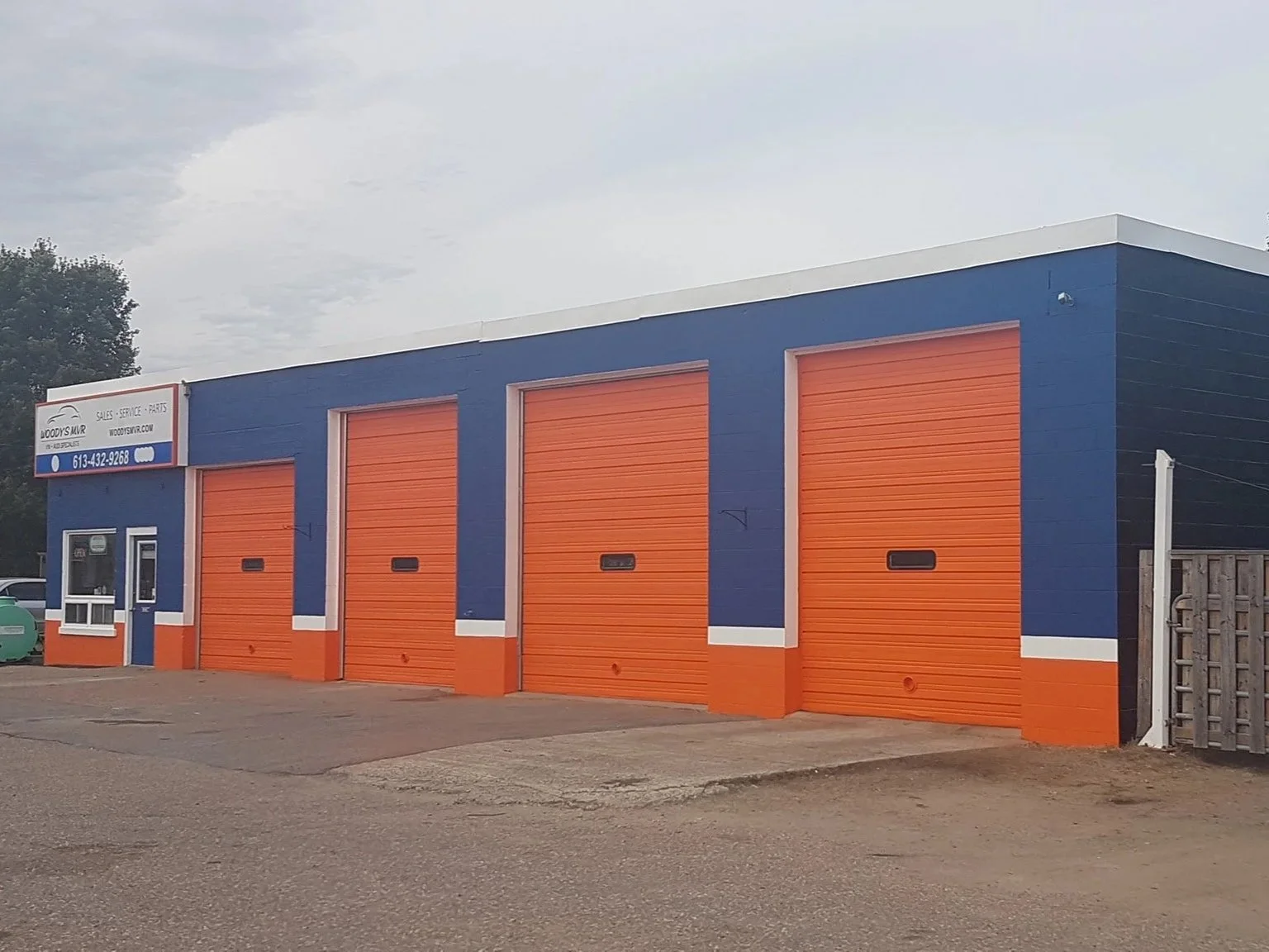 Colorful auto repair shop with four orange garage doors and blue walls, a small office area with a window and door, and a sign with contact info.