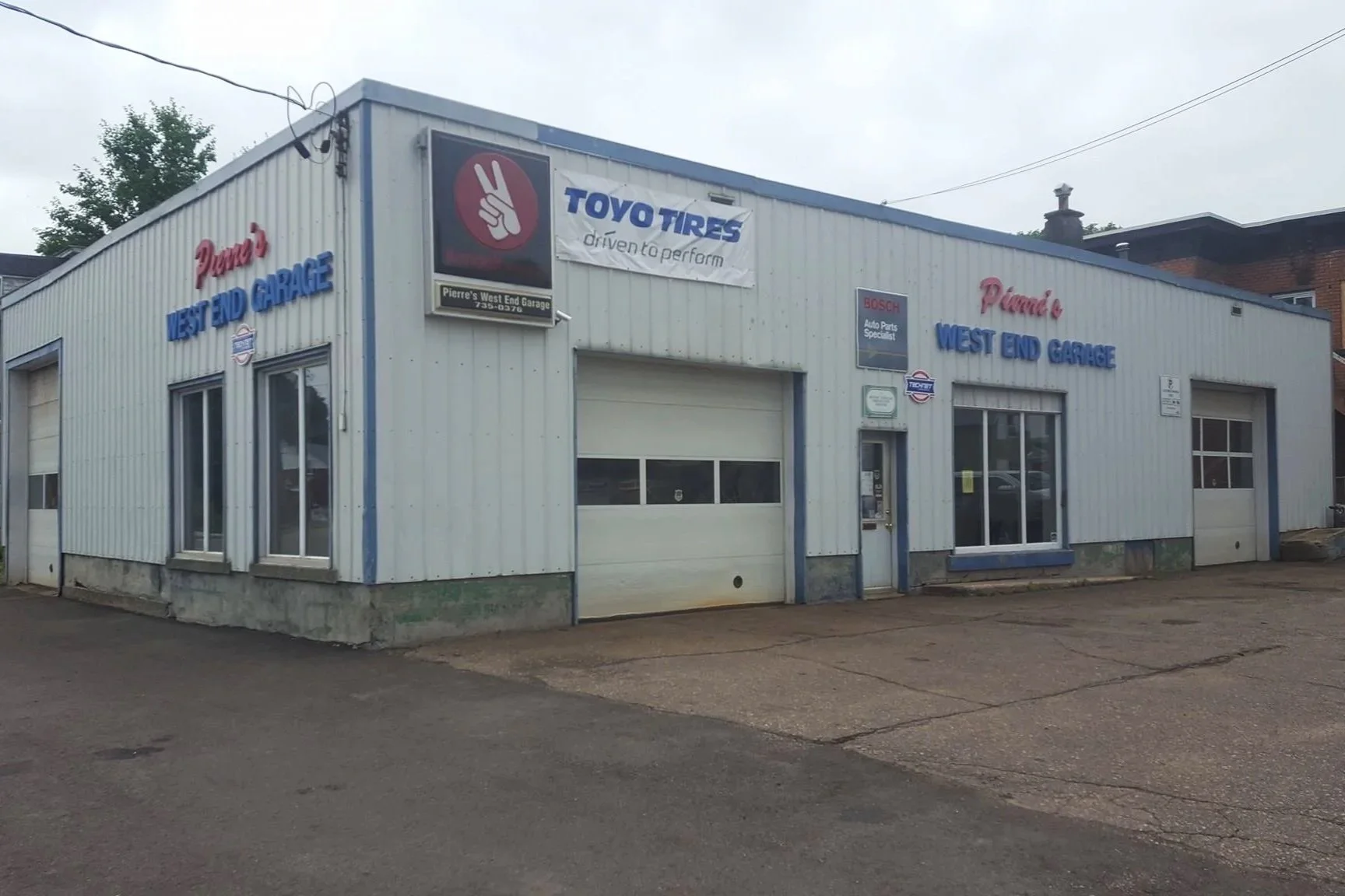 A garage building with signs for Piert's West End Garage, Toyo Tires, Bosch auto parts, and other logos, with a driveway in front.