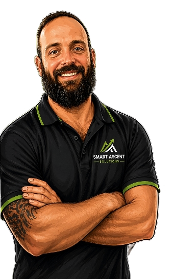 A man with a beard and mustache, wearing a black collared shirt with green accents and logo, smiling with arms crossed.