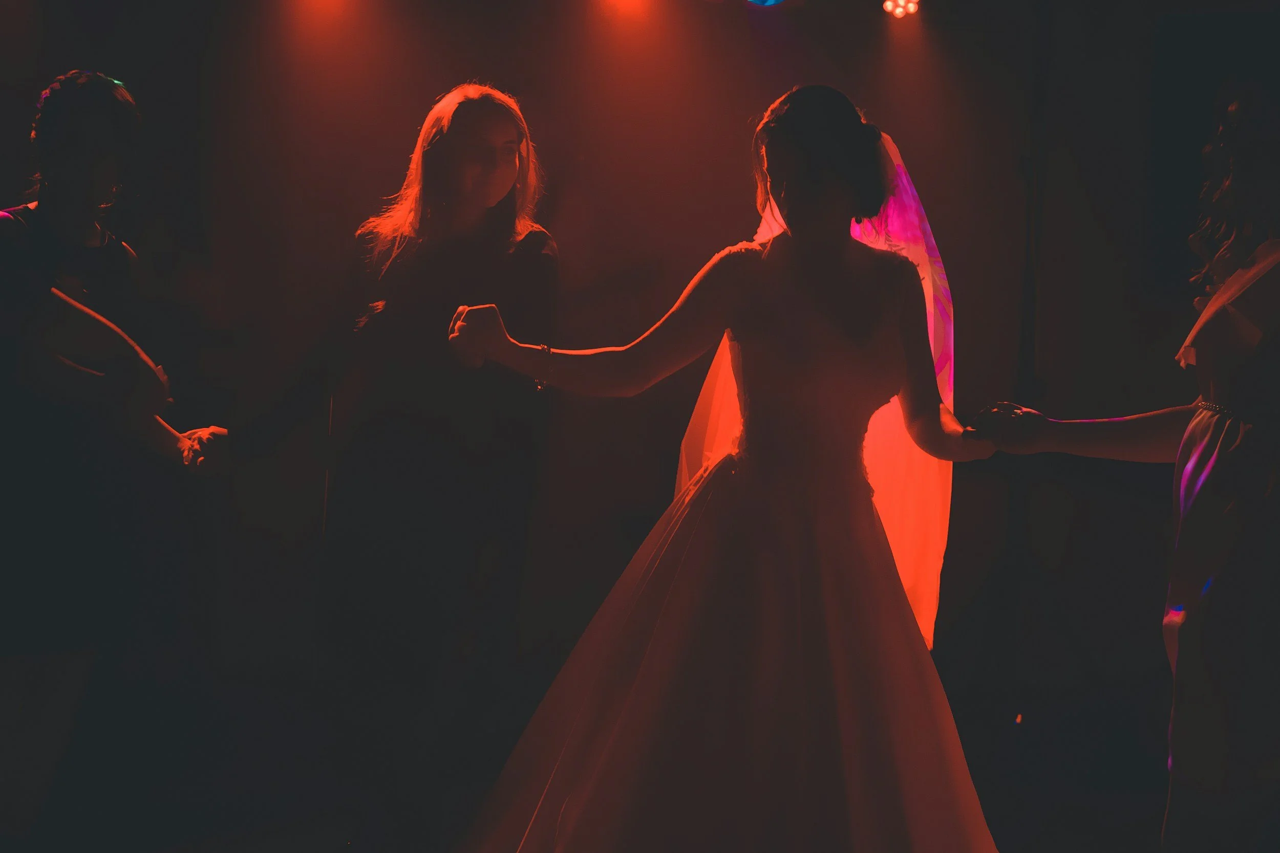Silhouettes of five women holding hands in a dark setting illuminated by red and purple stage lights.