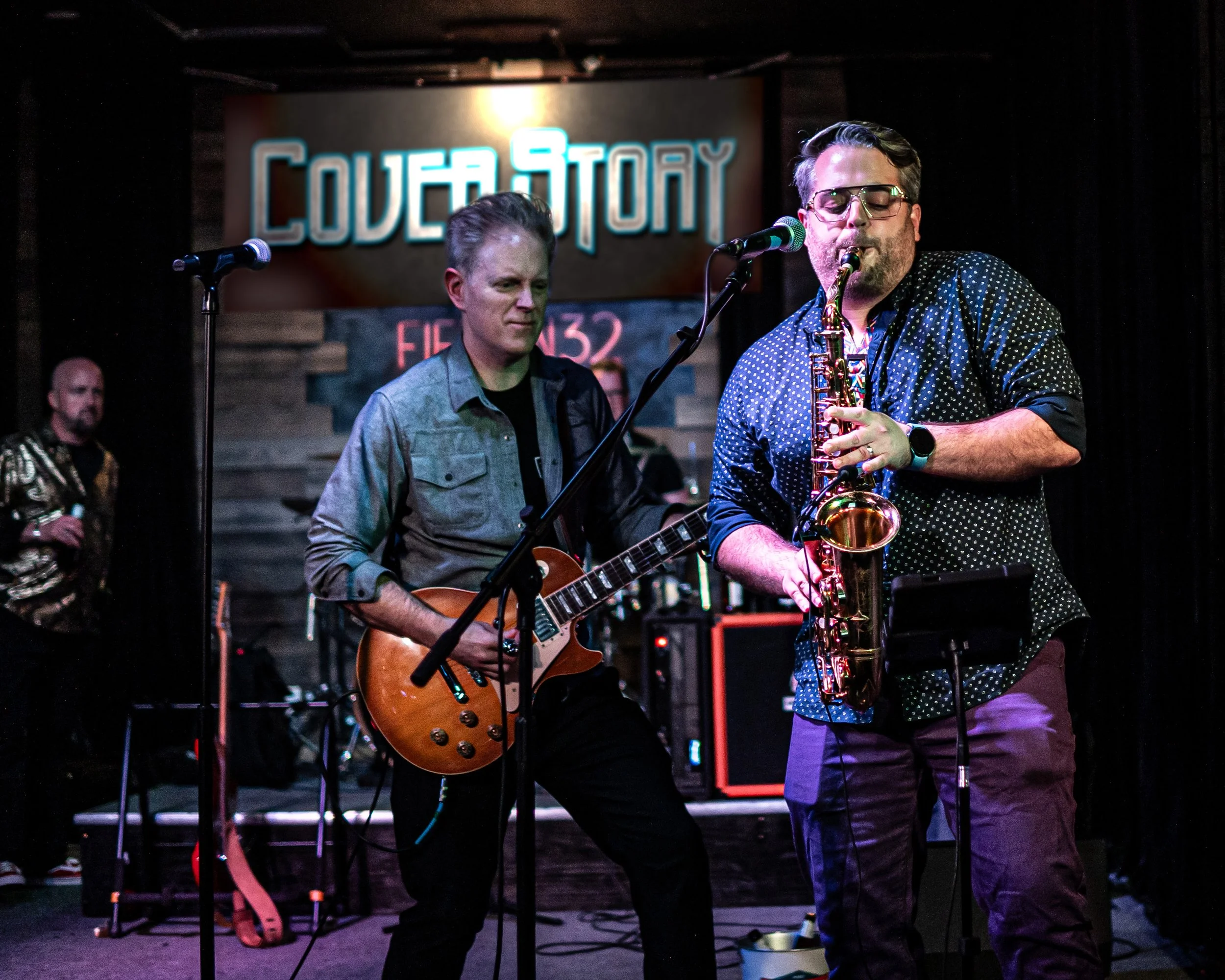 Musicians performing on stage with one playing the guitar and another the saxophone, at Covey Stony venue, with a sign behind them