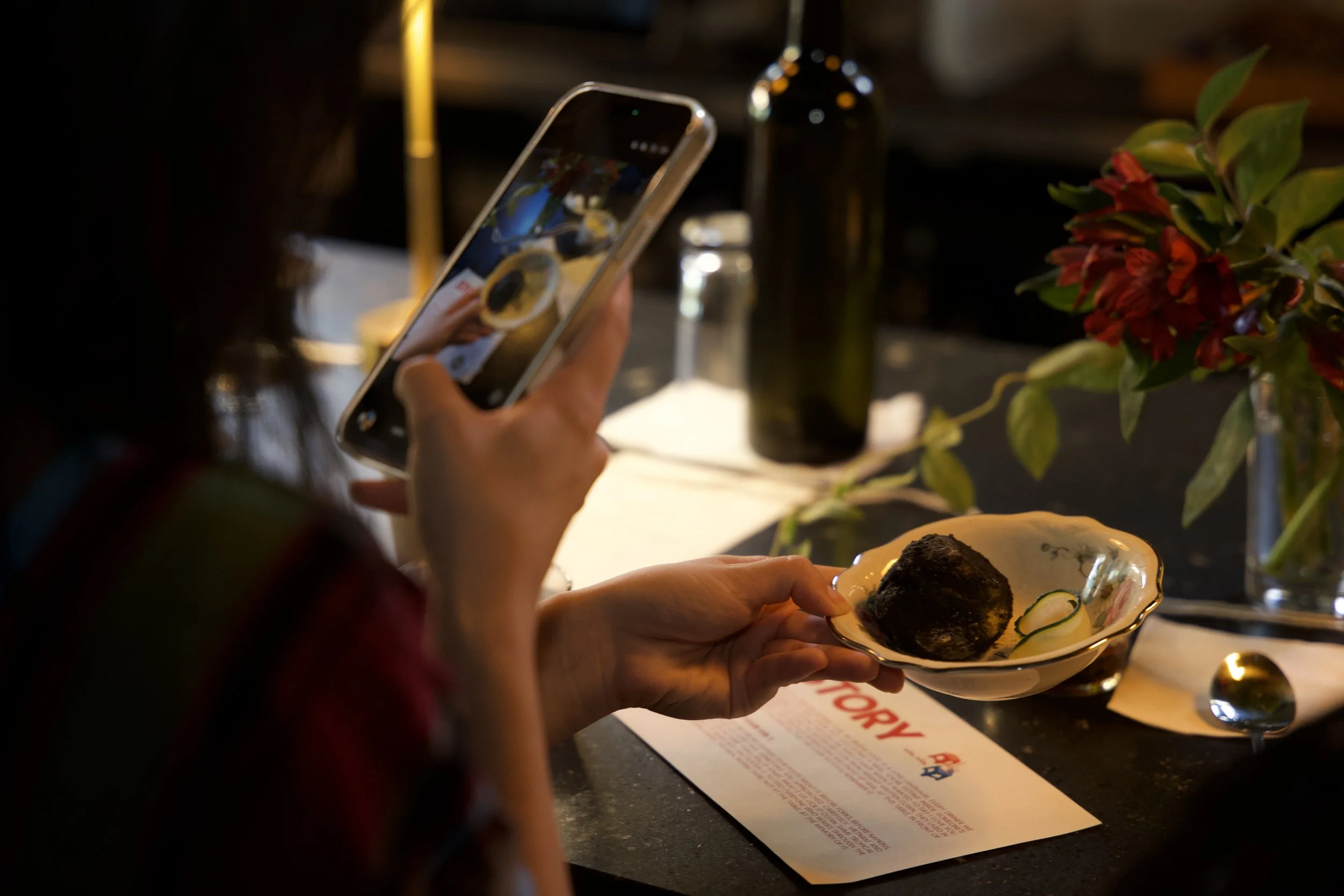 A patron takes a photo of Chef Andrea's pasteles de yuca, coated in an edible charcoal dust. Chef Andrea says the experience is to imitate dirt balls, like the ones you make as kids, except delicious. 