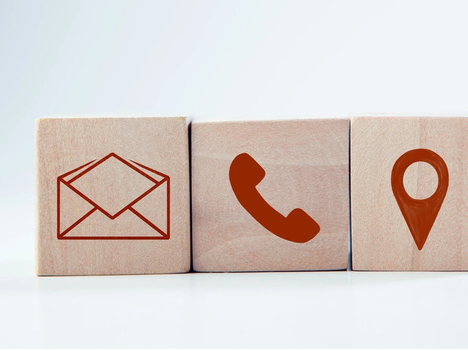 Three wooden blocks with icons: an envelope, a phone receiver, and a location pin, arranged horizontally.