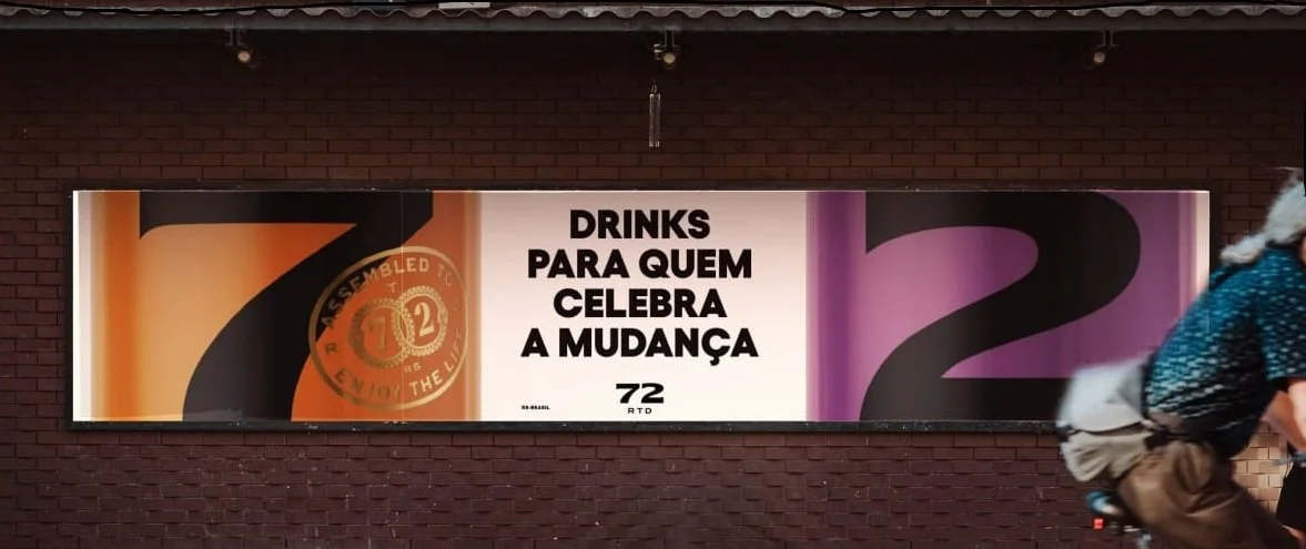 Faixa publicitária com mensagens em inglês e português relacionadas a bebidas e celebrações, com fundo de parede de tijolos.
