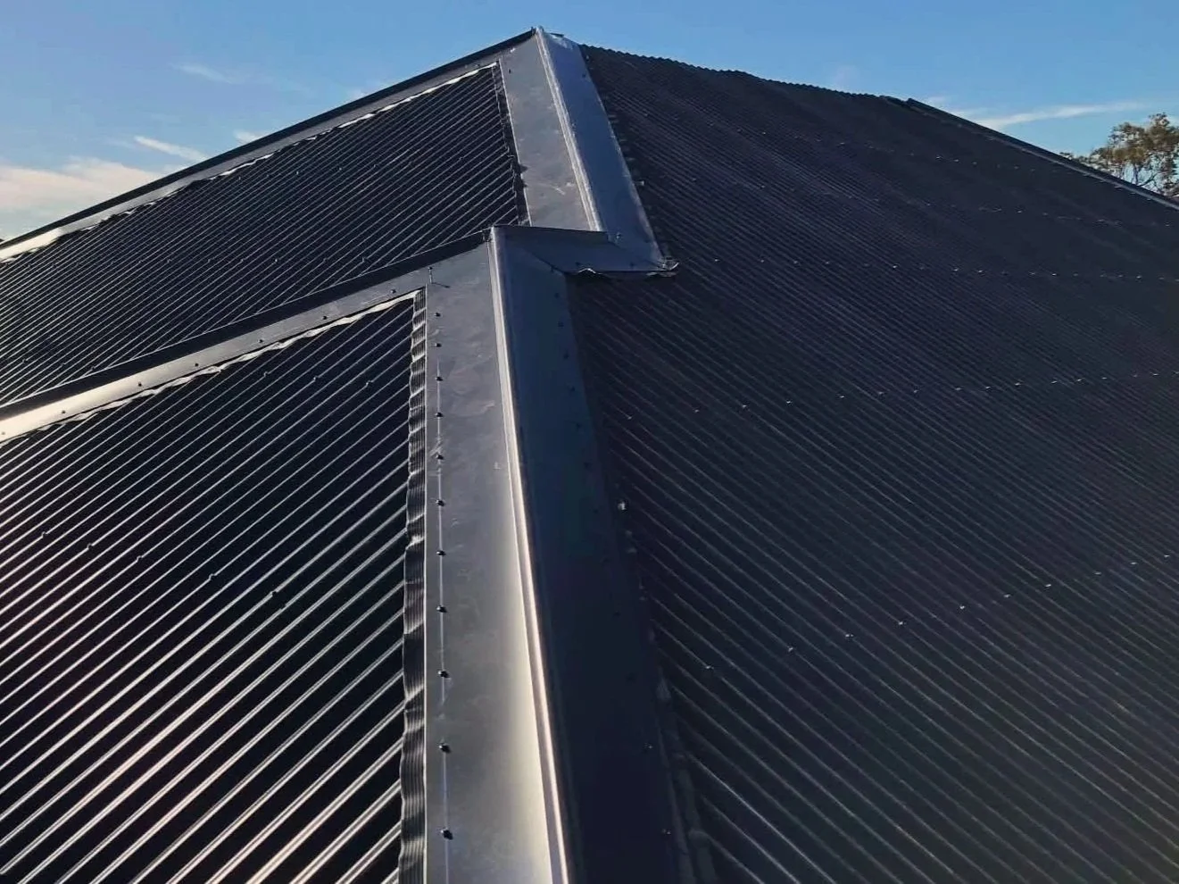 Close-up of a black iron roof with a metal ridge cap under a blue sky.