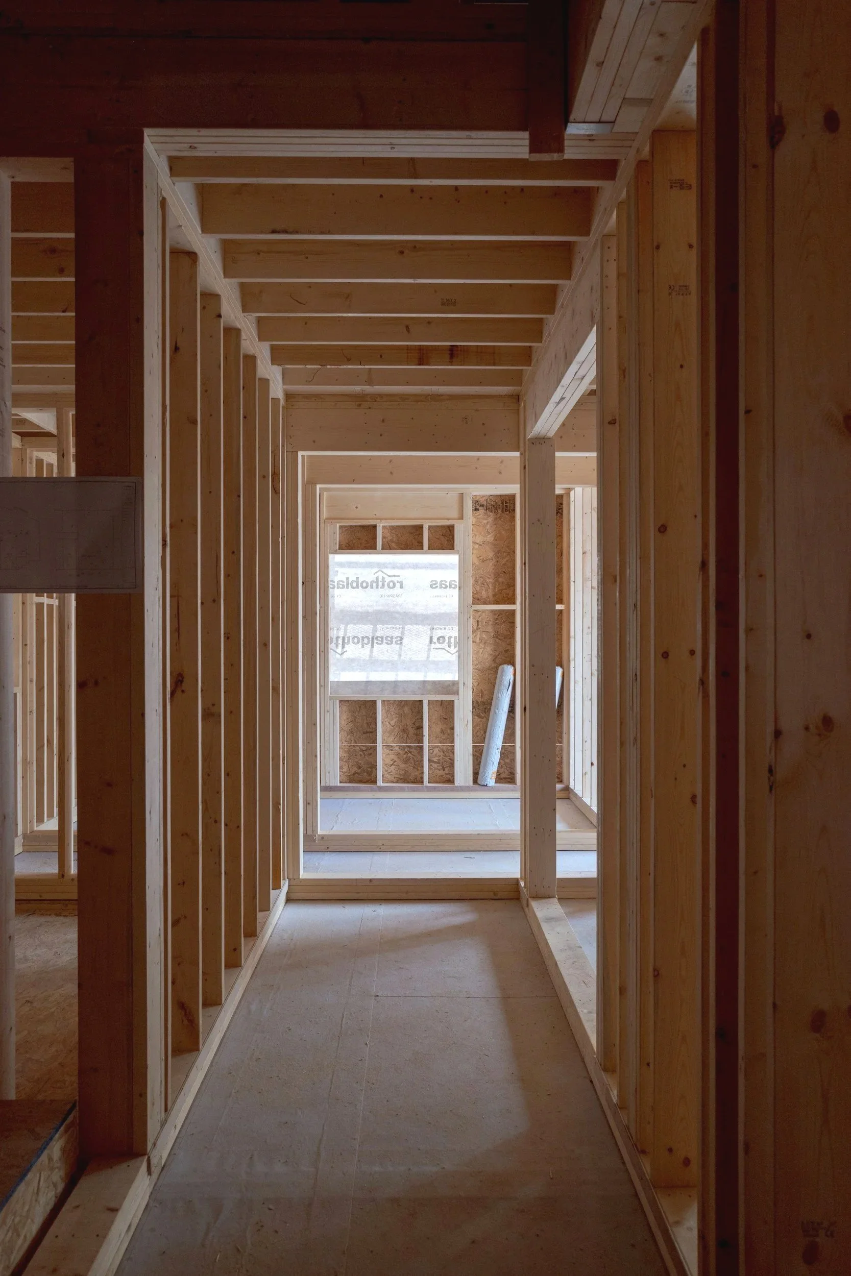 Wooden framing of a house under construction with exposed studs and beams, and wiring visible in some areas.