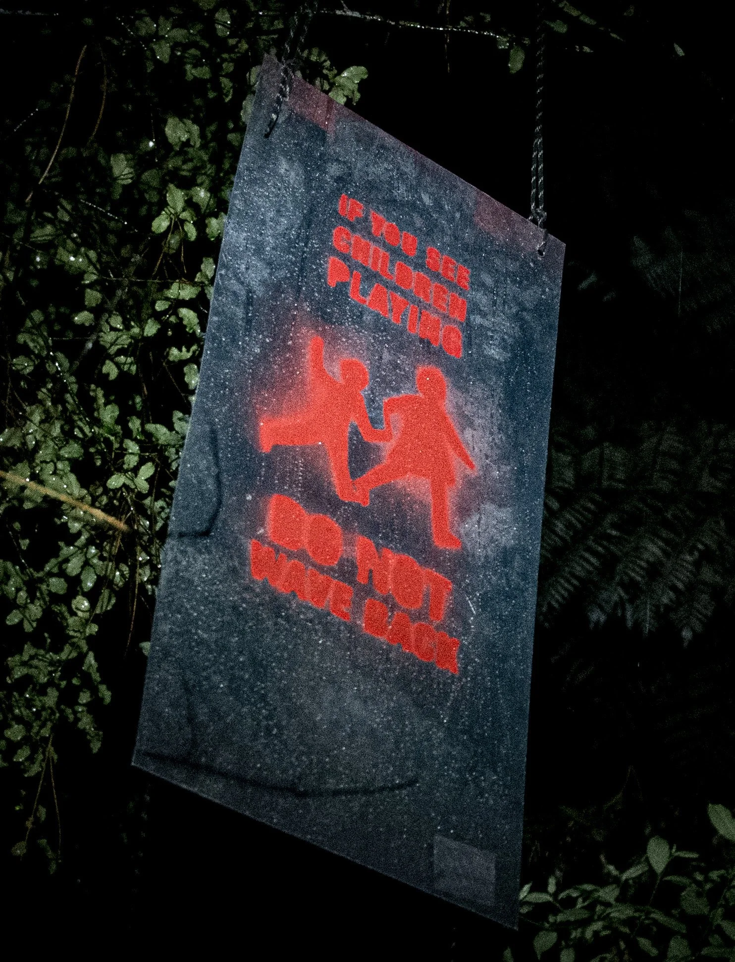 A mysterious sign hangs at night time, reading: If you see children playing, do not wave back.