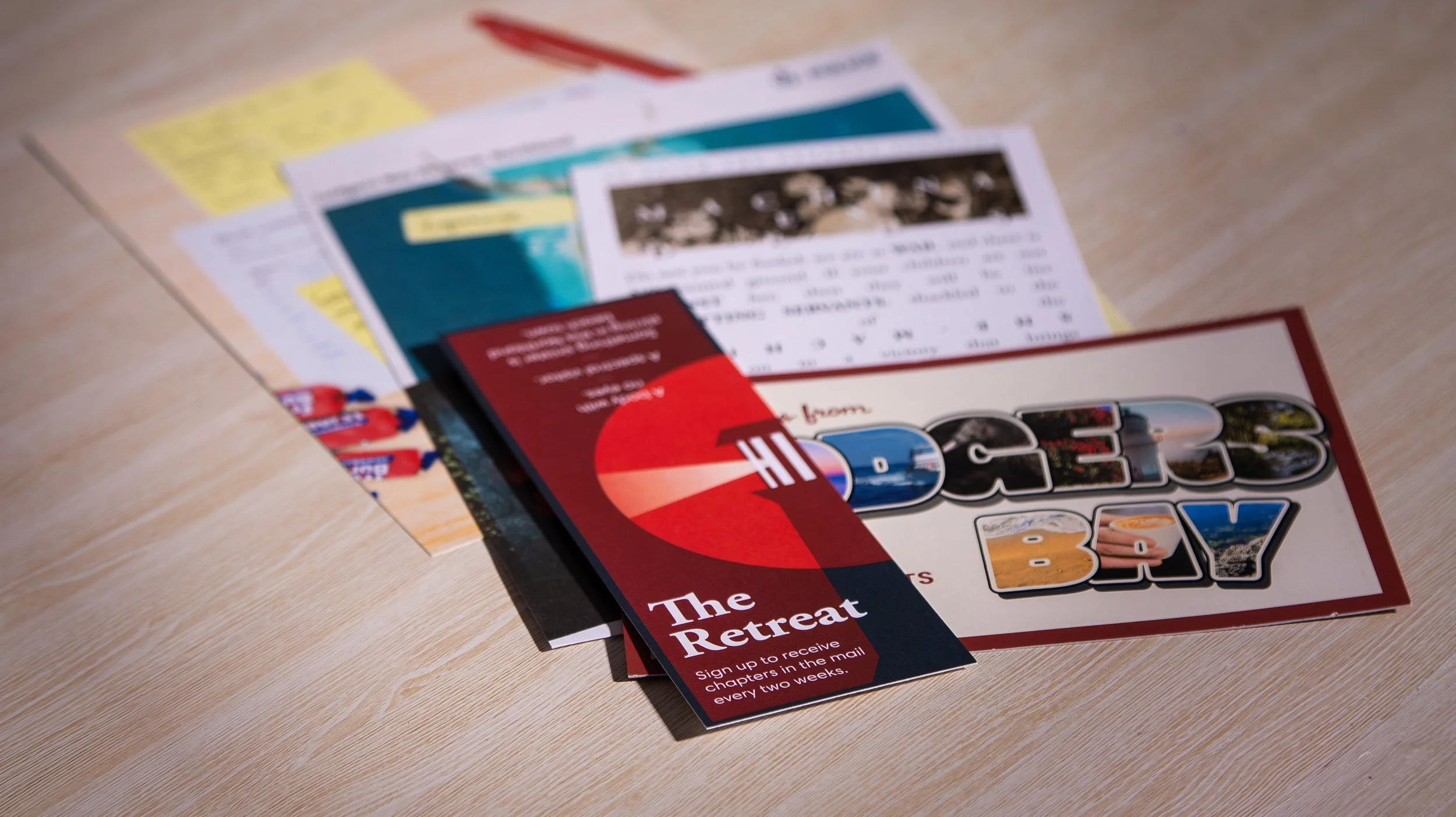 Blurred brochures and pamphlets on a wooden table, including one with the title 'The Great Retreat' with images of a lake and a sand dune.