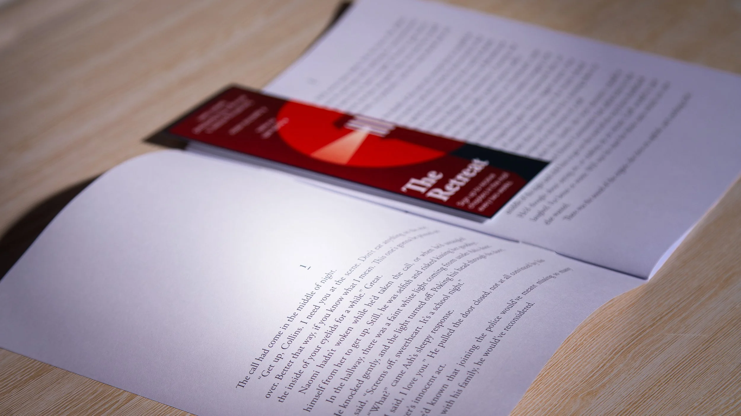 A pamphlet titled 'The Redacted' on top of an open printed story, placed on a wooden table.