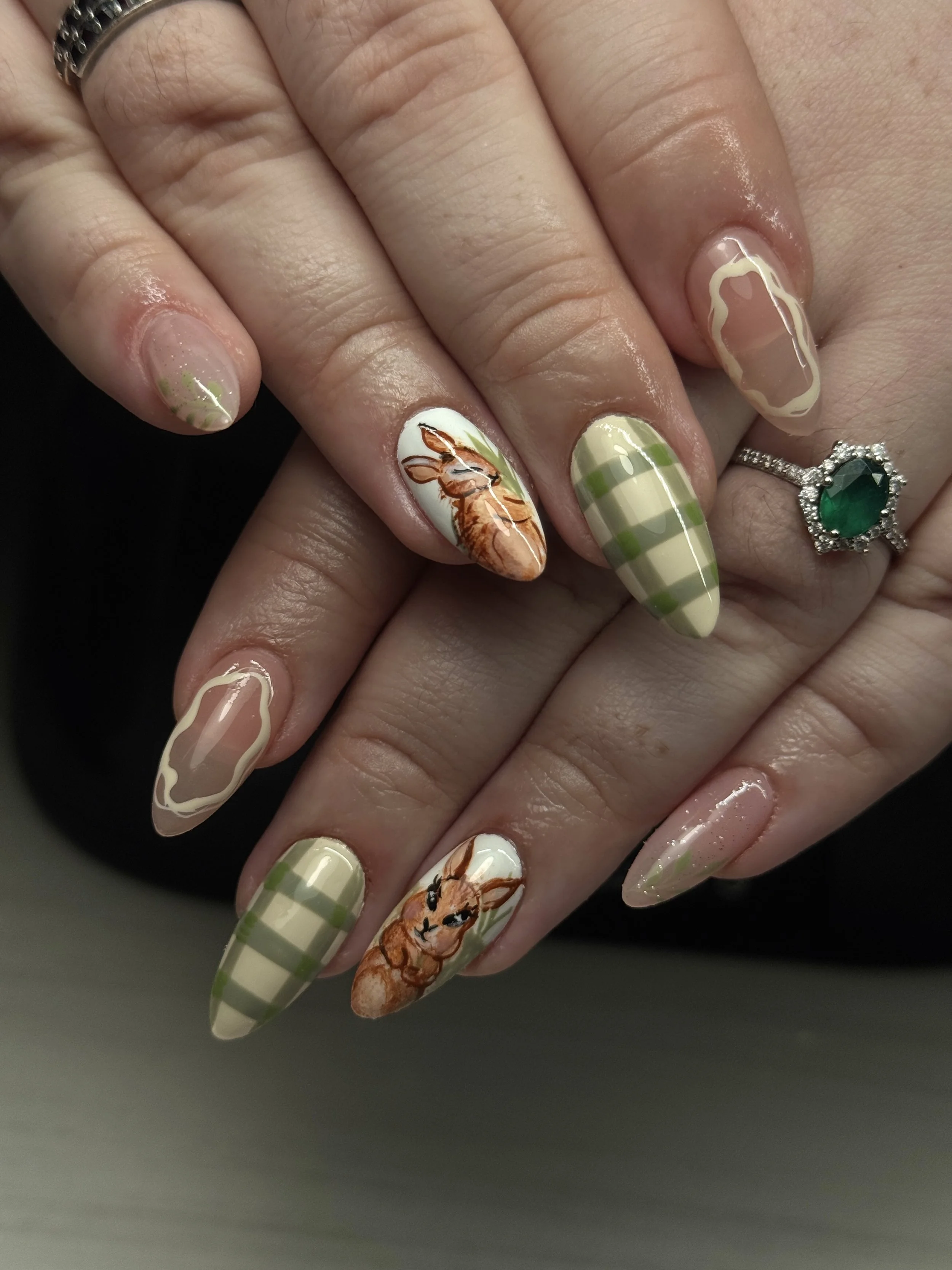 Nail art with bunny and deer illustrations, pink and green plaid patterns, and abstract outlines on natural-colored nails.