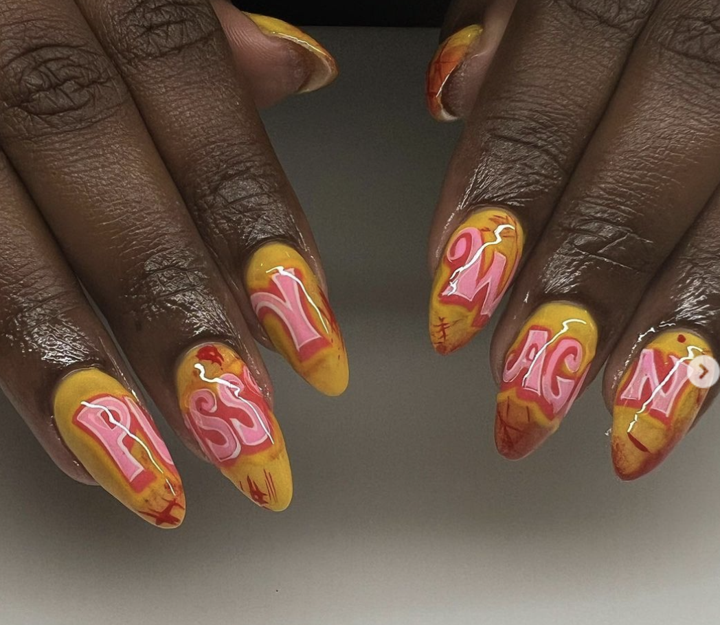 Nail art design with yellow and red marbling and pink letters spelling out 'Pussy Wagon"