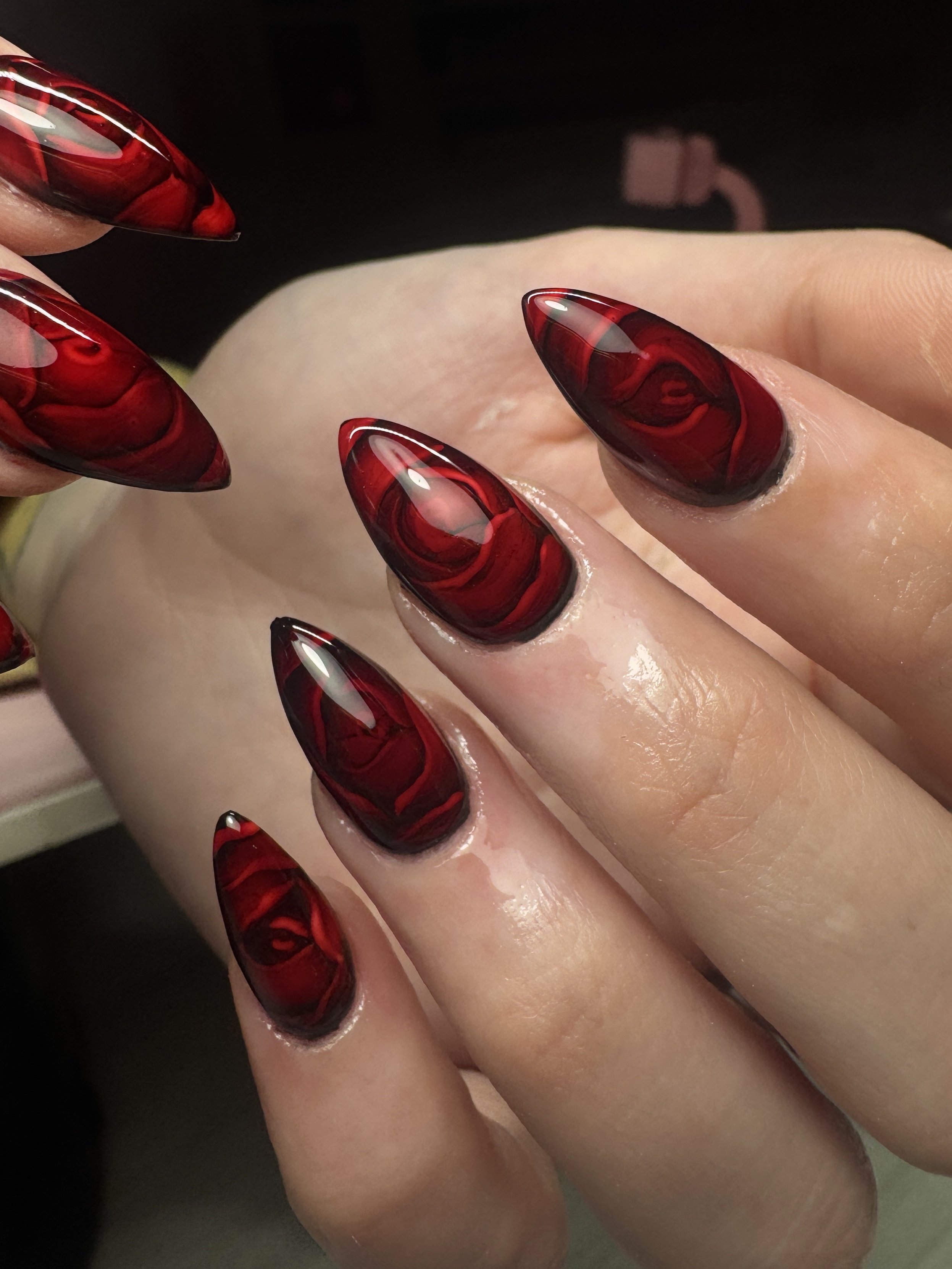Close-up of a hand with long, almond-shaped red and black marbled acrylic nails.