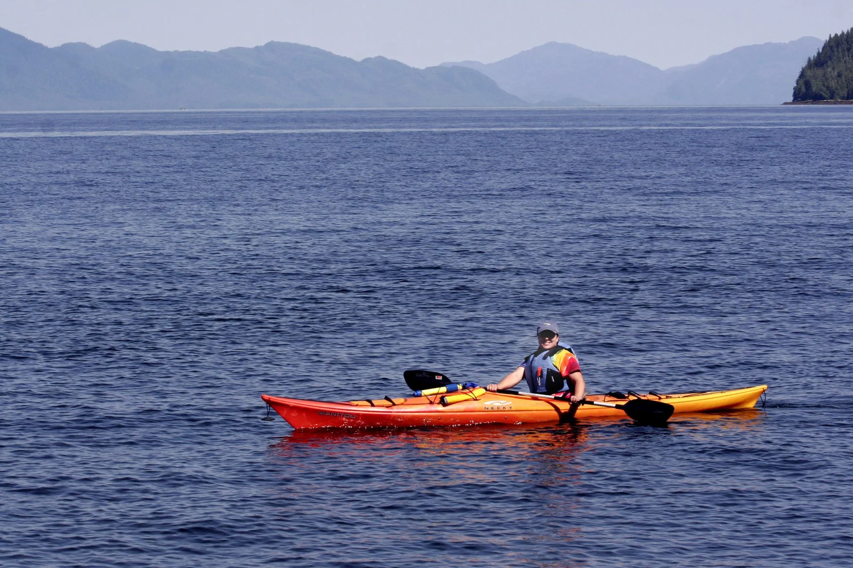 Person kayaking on a large body of water with mountains in the background.