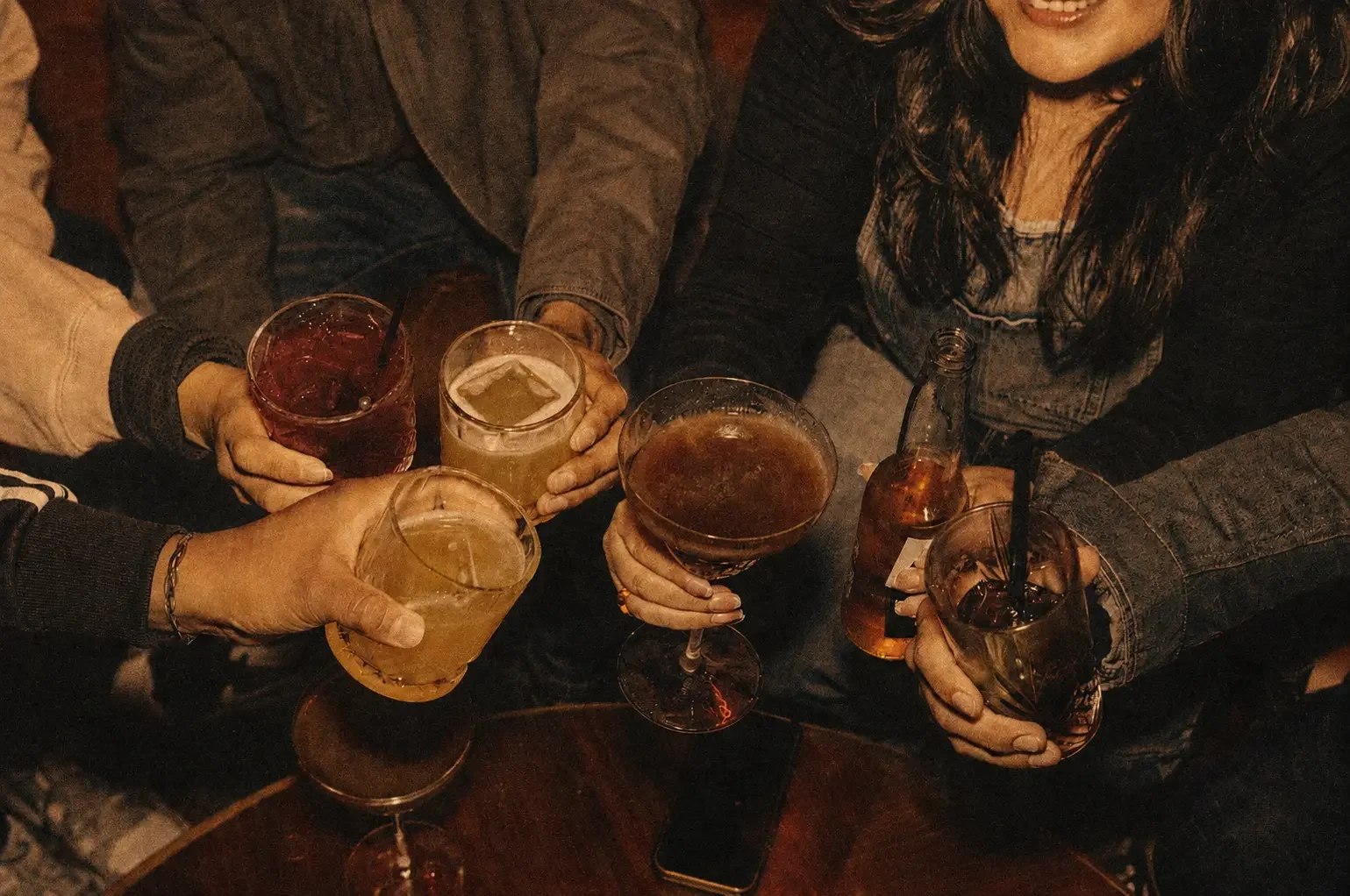 Group of friends holding drinks at a social gathering in a dimly lit setting.