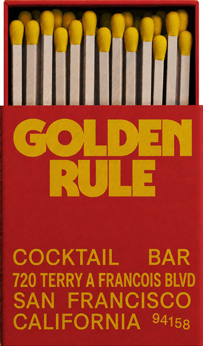 A box of matches with yellow heads and white sticks, with the brand name 'GOLDEN RULE' in large yellow letters and the address of a cocktail bar in San Francisco printed on the box.