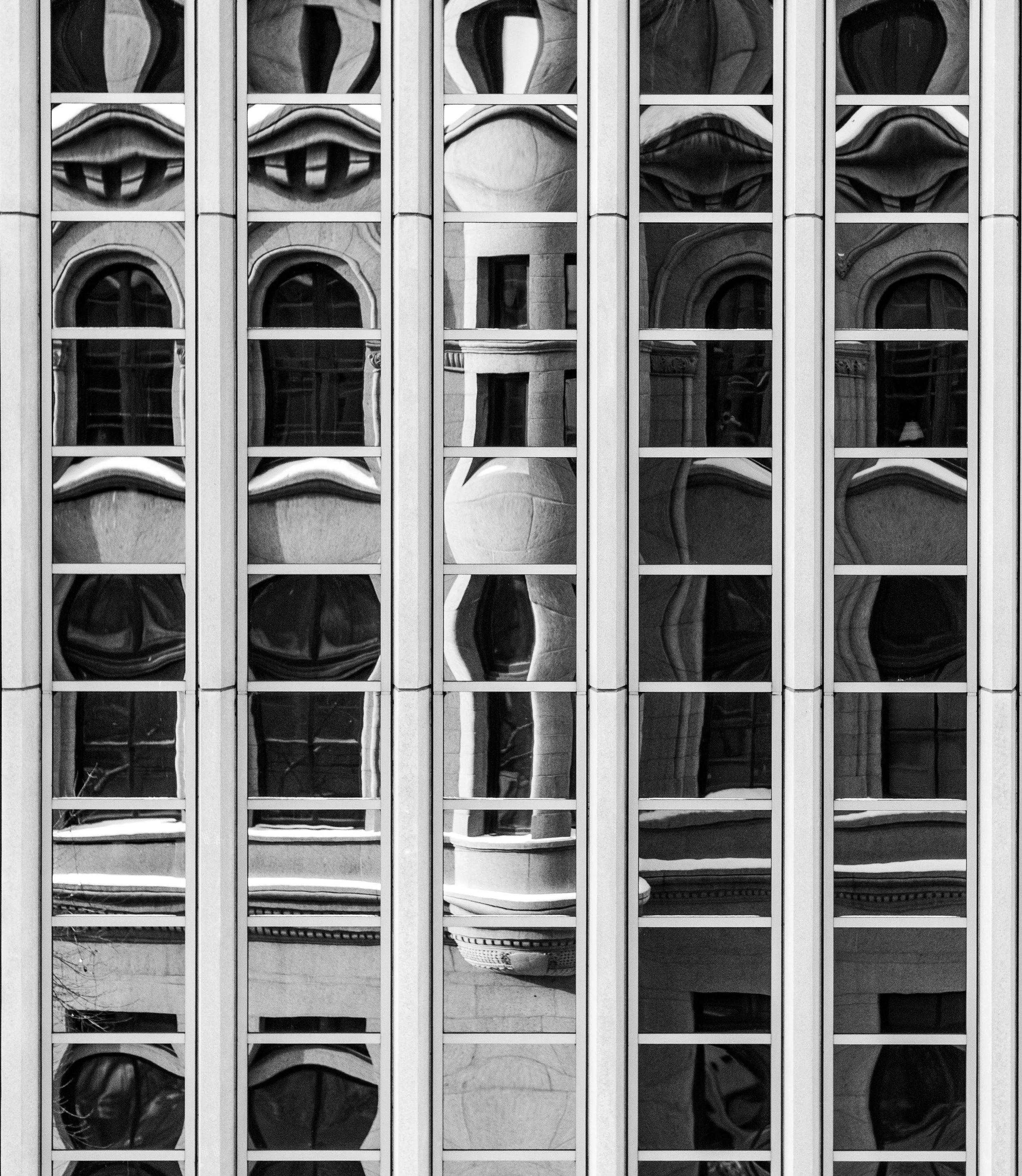 Reflection of a building's ornate facade and sky on the glass windows of a modern office building with vertical window frames.