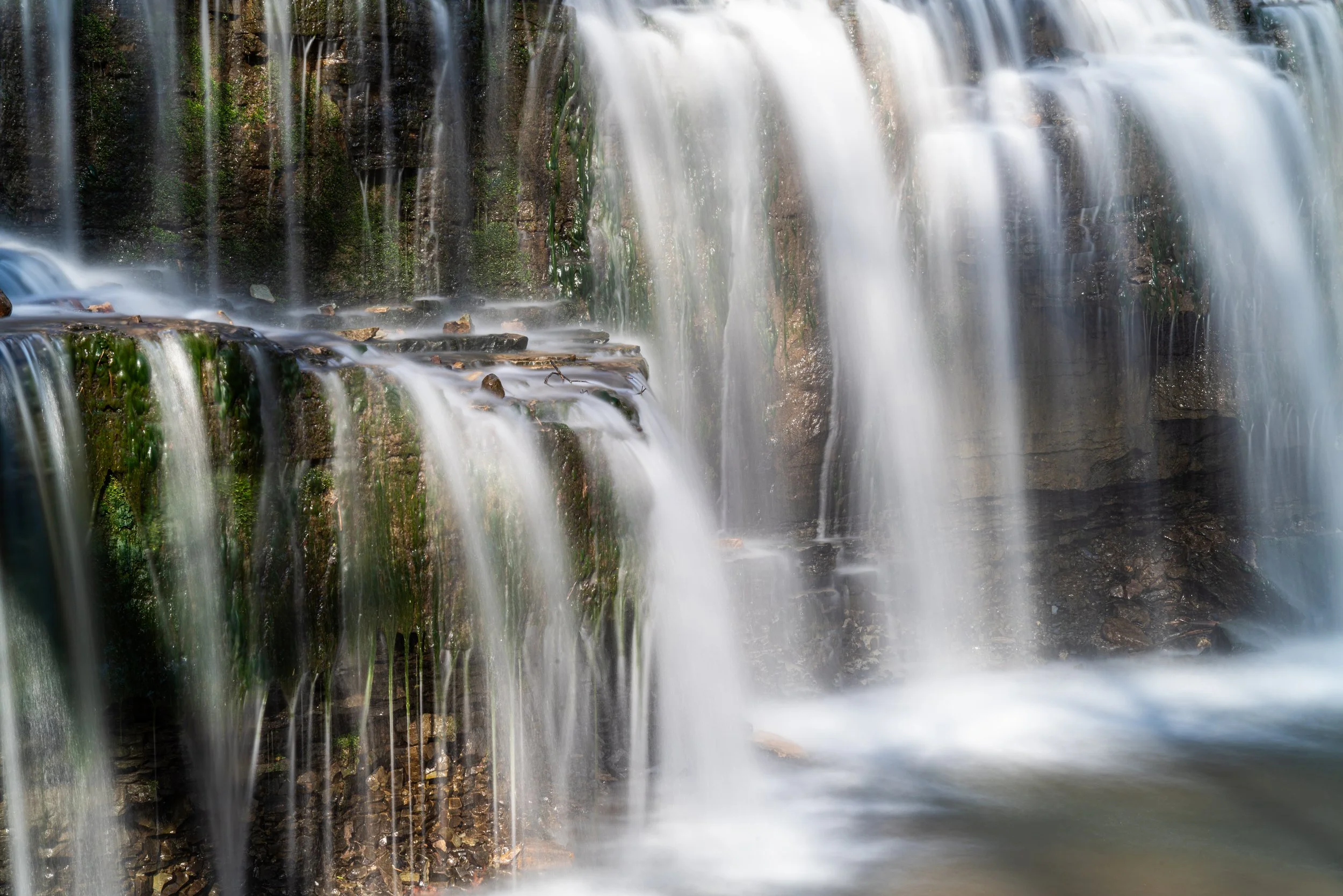A cascading waterfall flowing over rocks and moss in a natural forest setting.