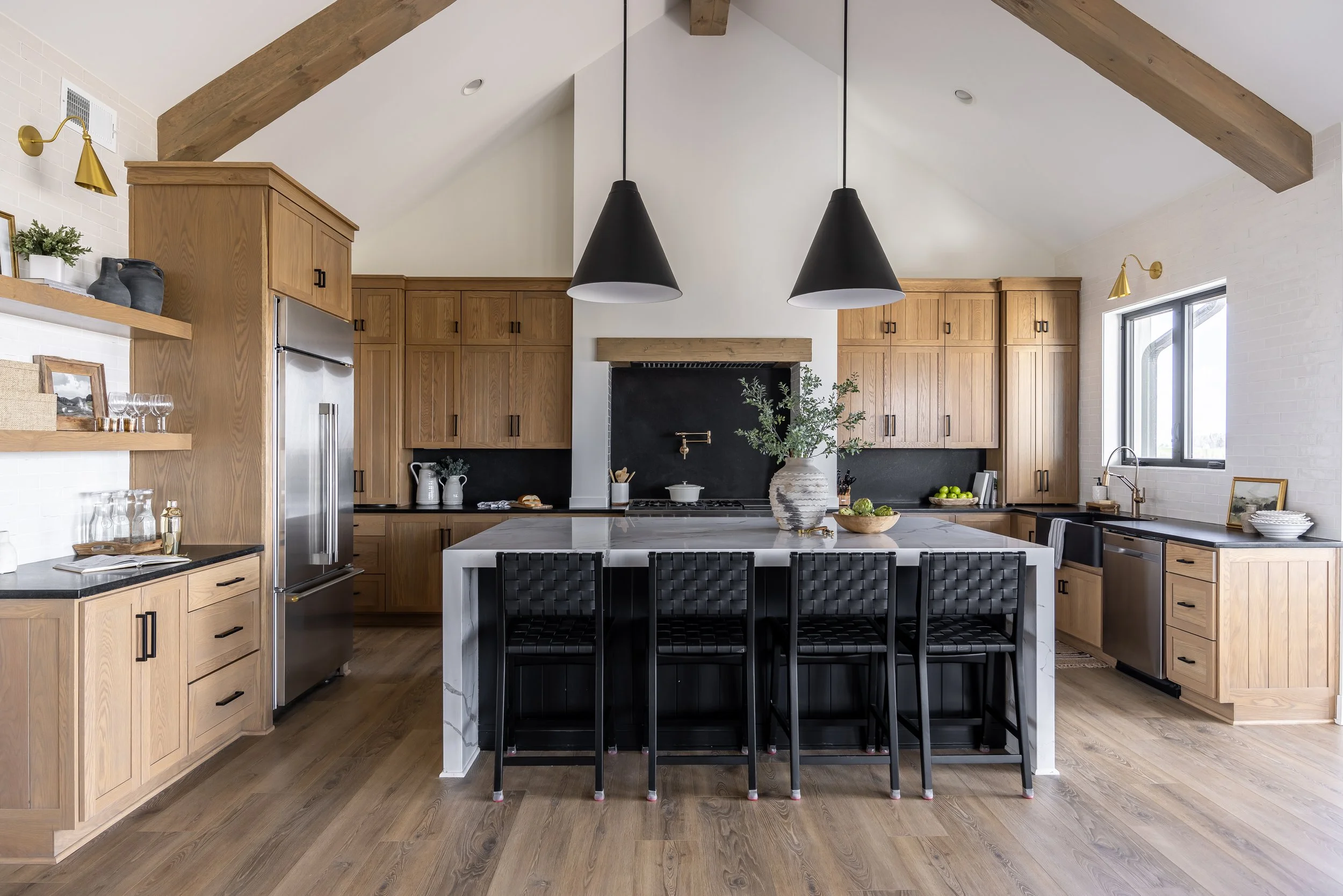 Modern kitchen with wood cabinets, a large white island, black pendant lights, and a gray dining chairs.