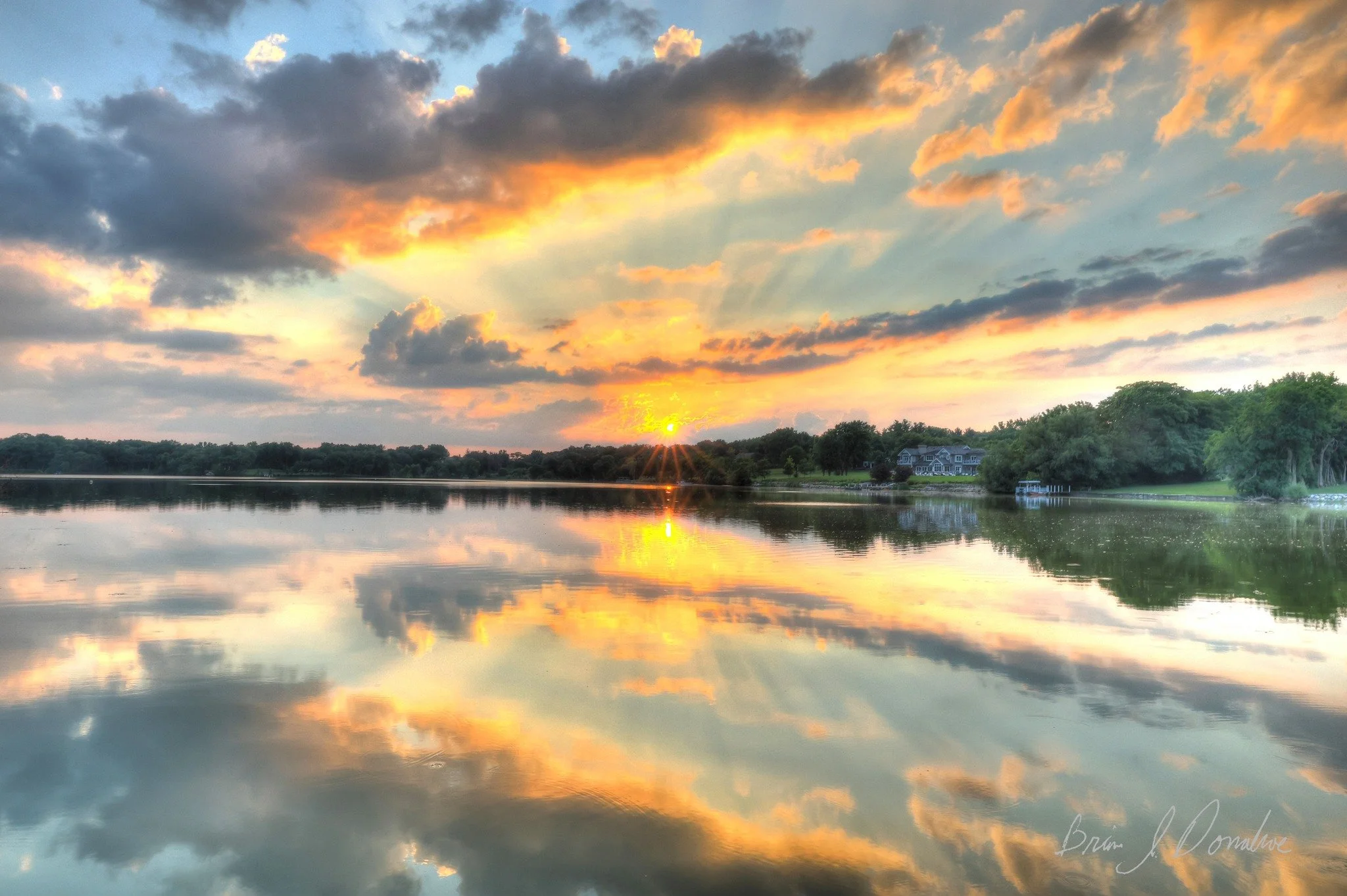 Sunset over a calm lake with reflections of clouds and trees