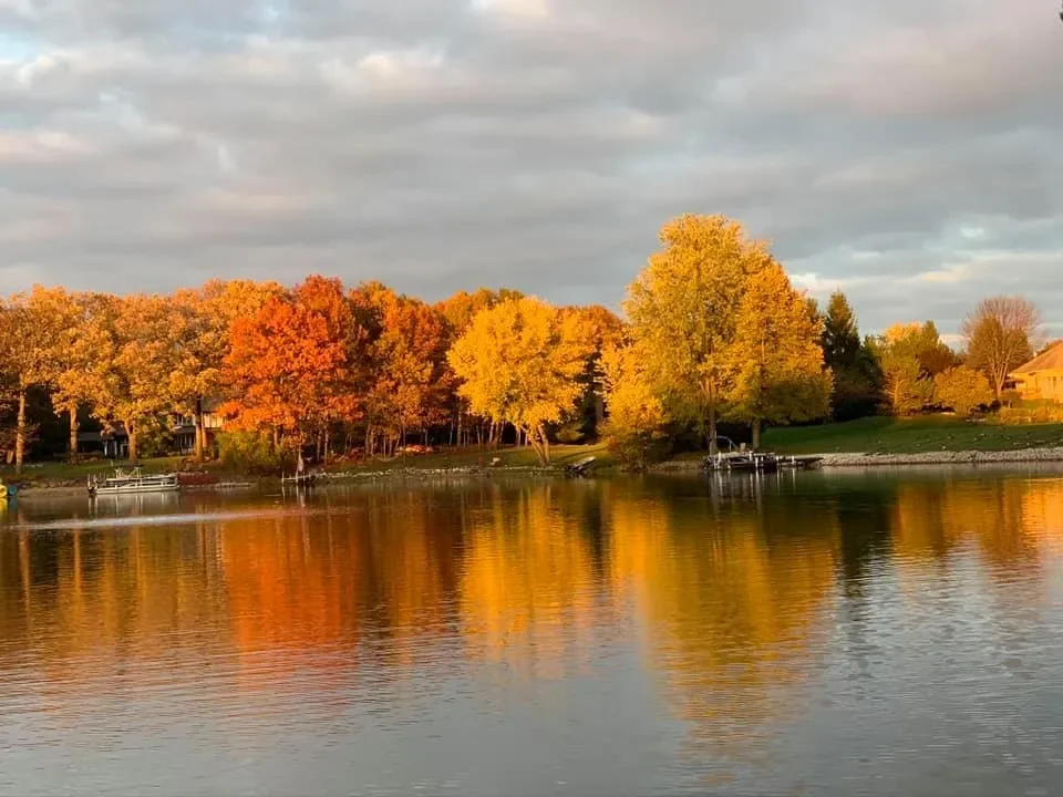 A peaceful Countryside Lake reflecting colorful autumn trees with orange, yellow, and green leaves, under a cloudy sky.