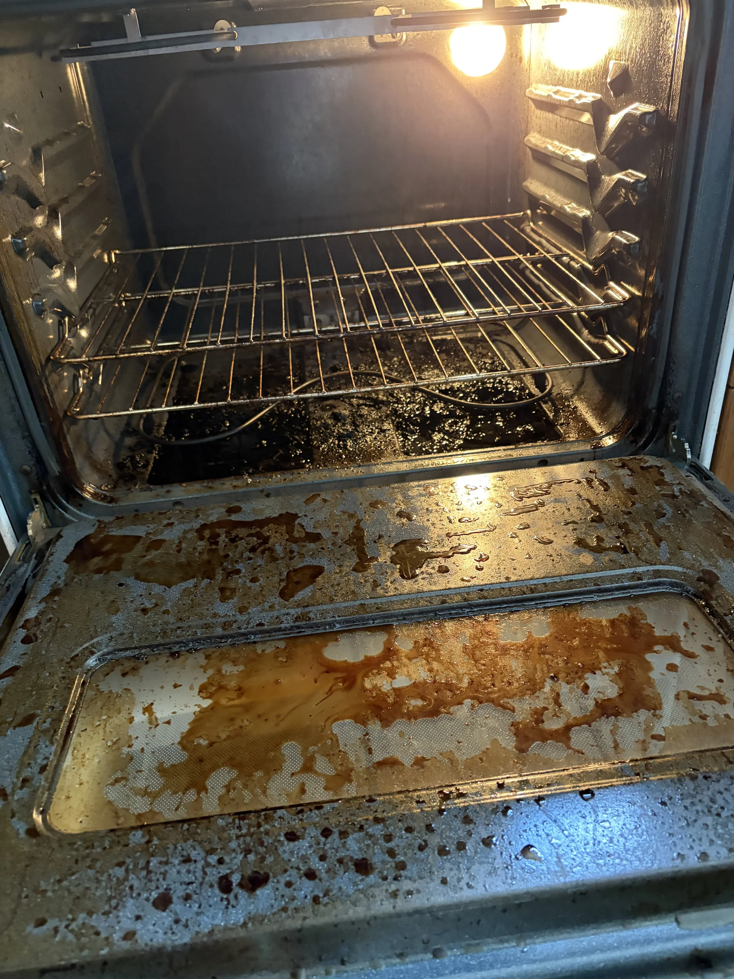 Empty oven with burnt food and grease on the oven racks and bottom surface.
